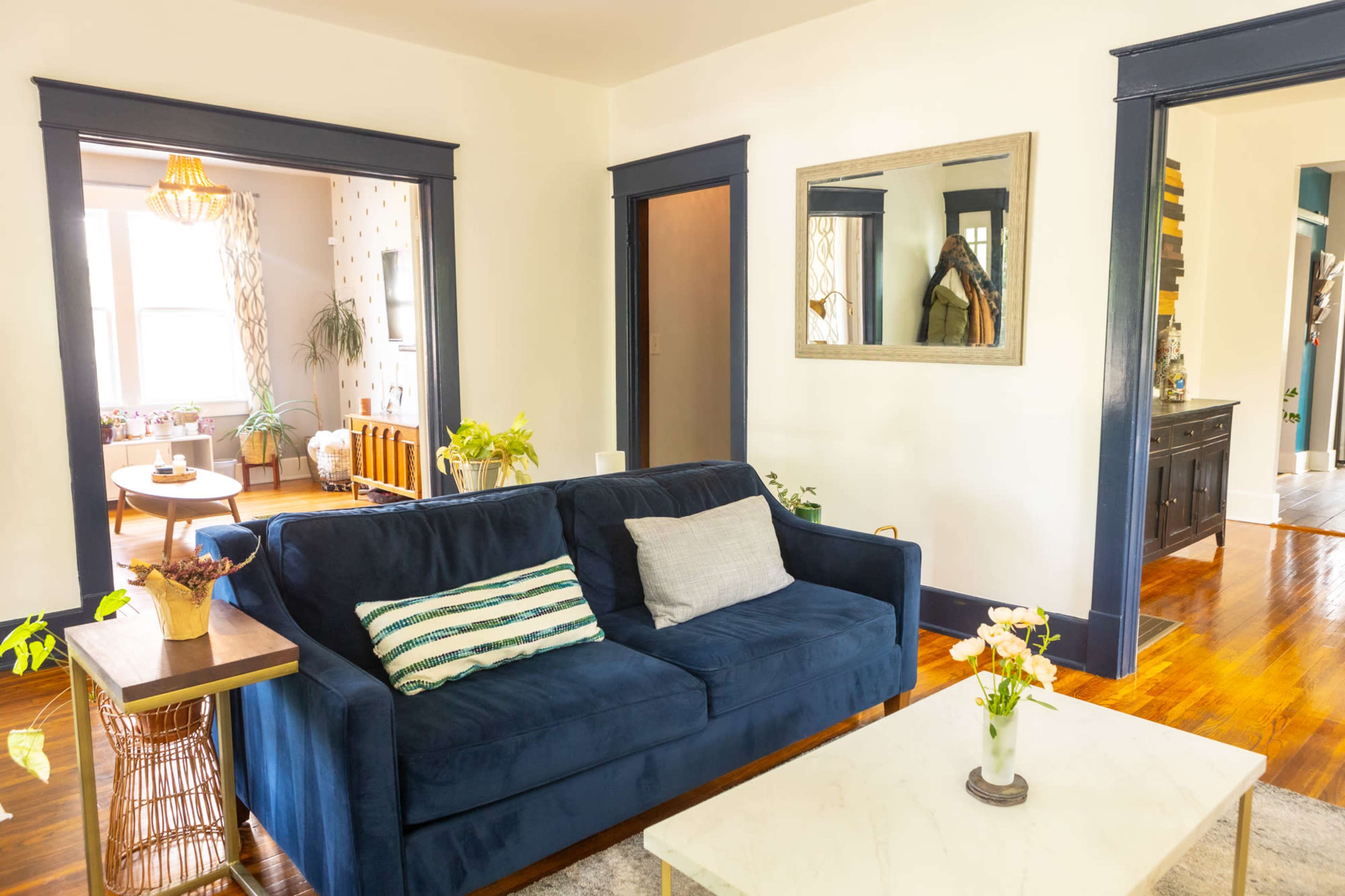 A blue sofa with decorative cushions is positioned in a living room with wooden floors and two doorways leading to adjacent rooms.