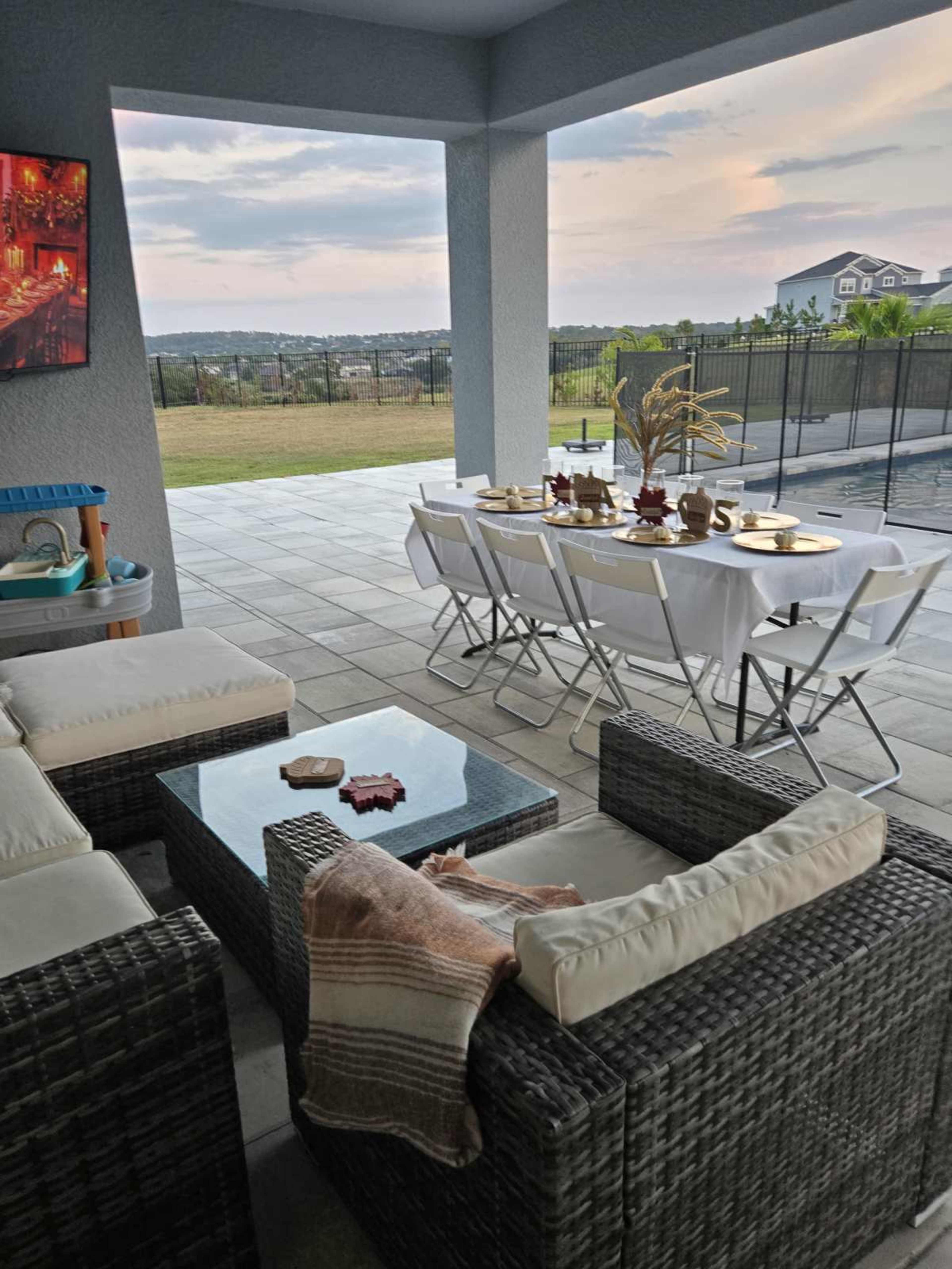 A patio area features a seating arrangement with wicker furniture and a dining table set for a meal, overlooking a scenic view.