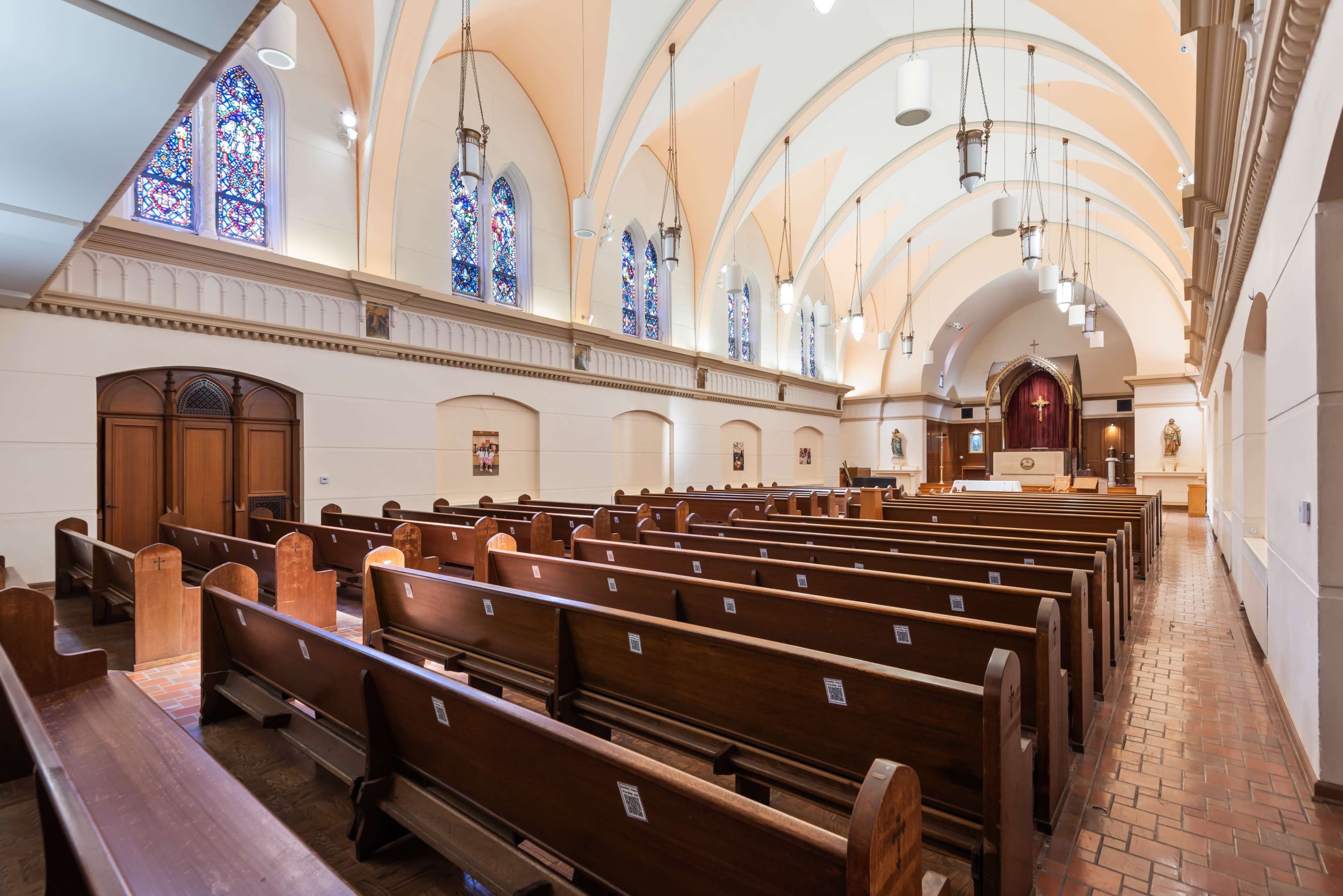 The image shows the interior of a church featuring wooden pews, arched ceilings, and stained glass windows.