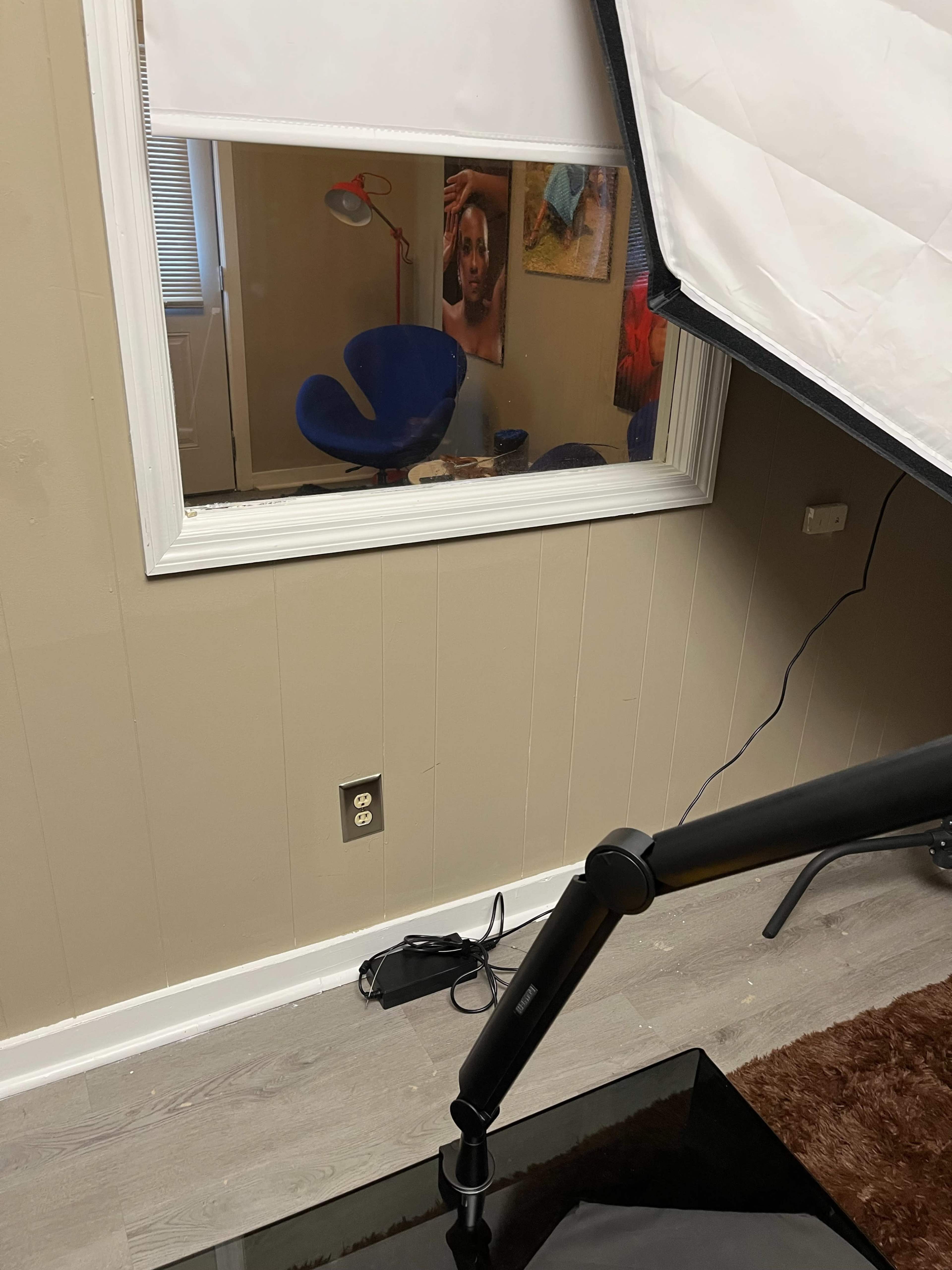 A window is visible with a blue chair and a lamp inside the room, while a large softbox is positioned outside.