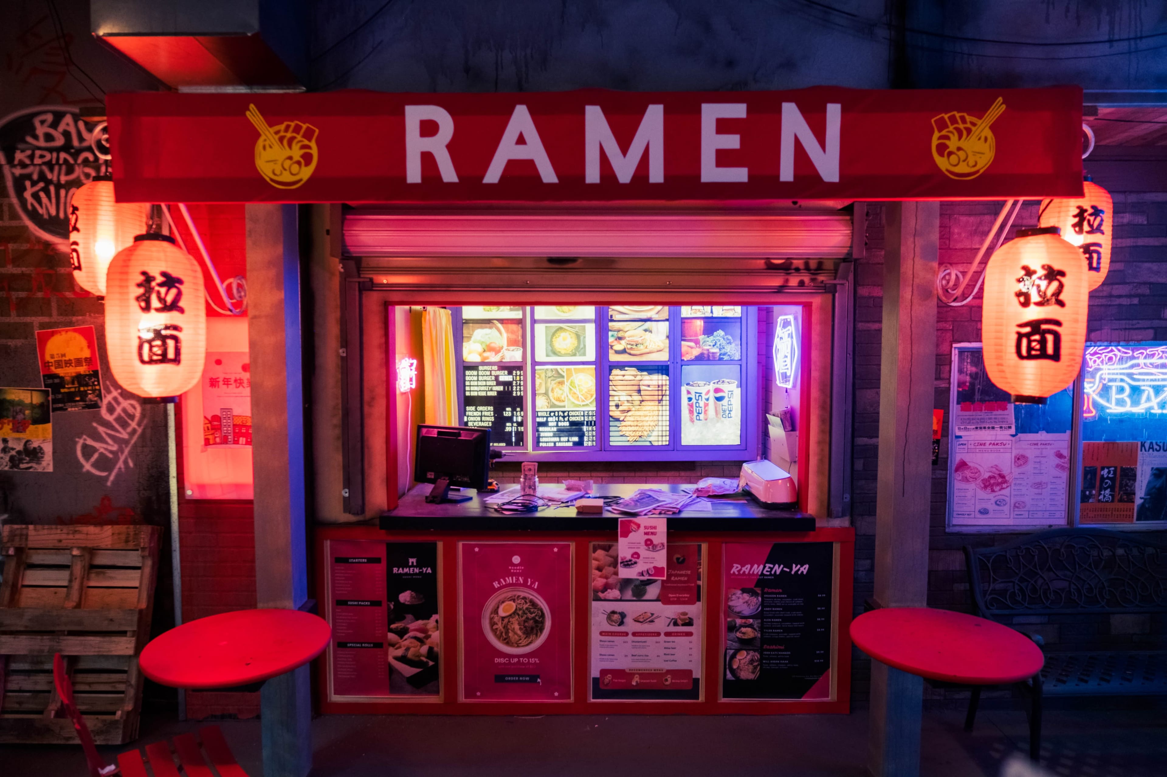 A ramen stall with a bright red sign, illuminated lanterns, and a menu displayed in the window.