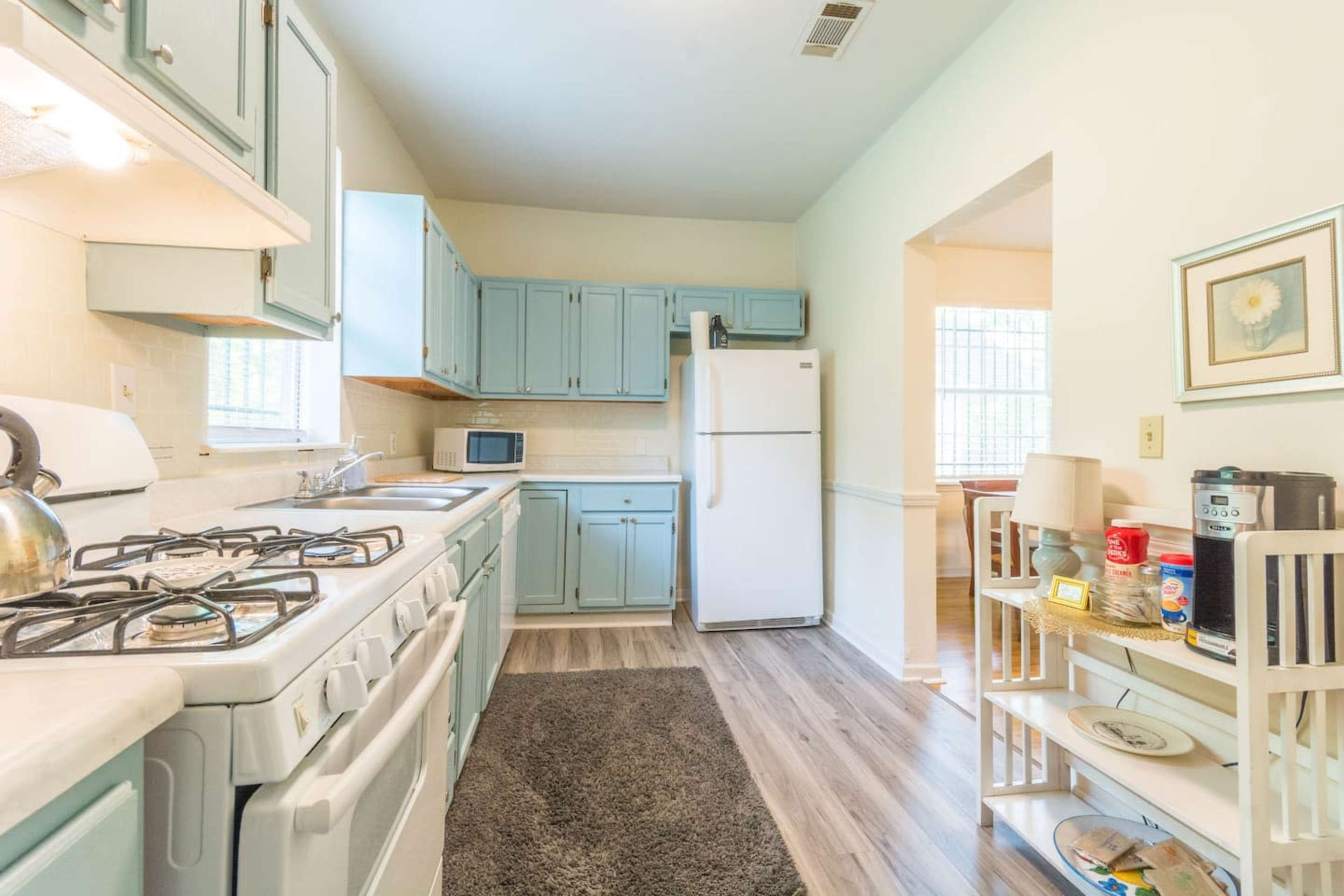 The kitchen features light blue cabinetry, a white stove and refrigerator, and a small table with items on it.