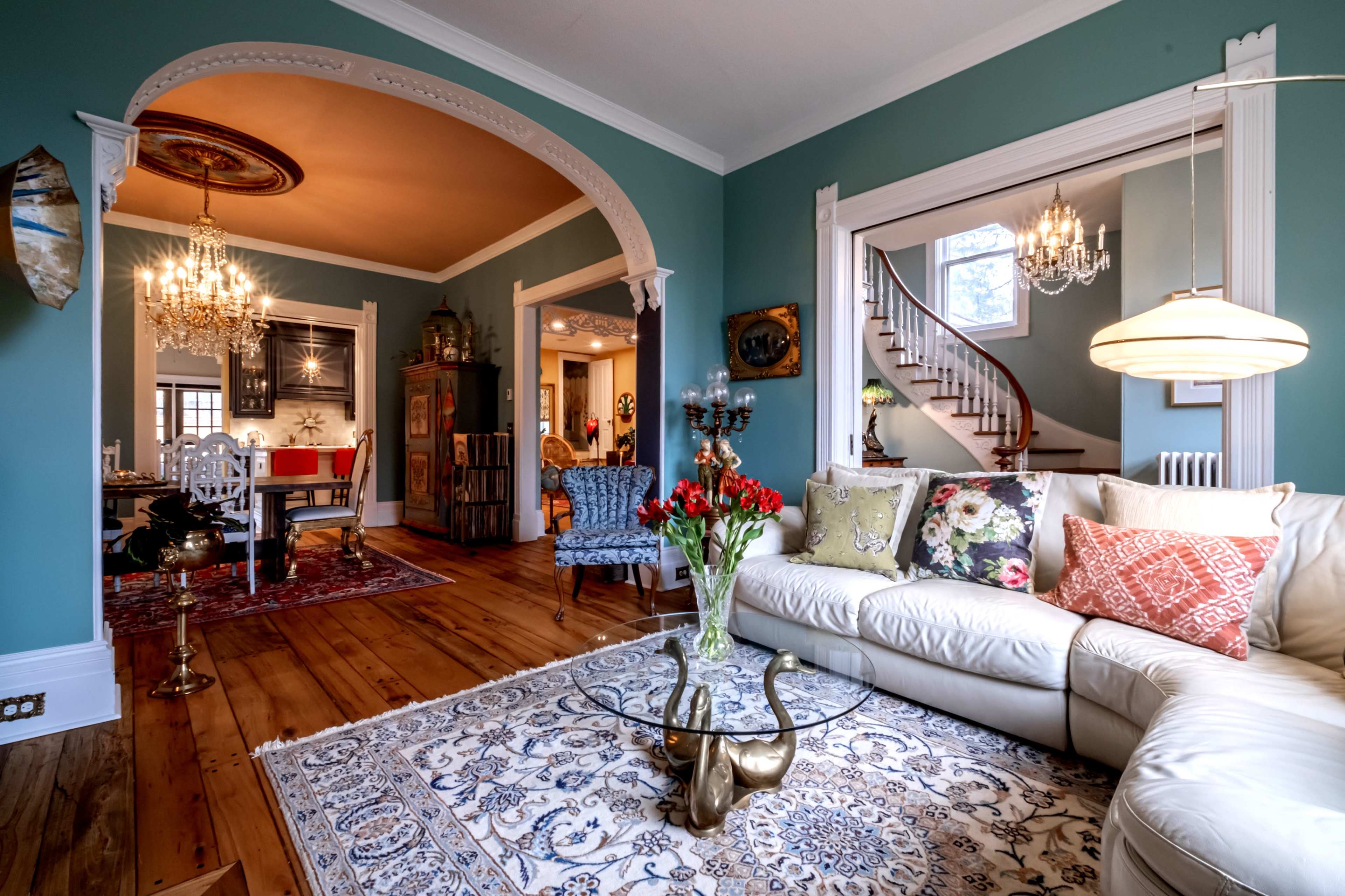 A stylish living room with a light-colored sofa, a glass coffee table, and a decorative rug, leading into a dining area and a staircase.