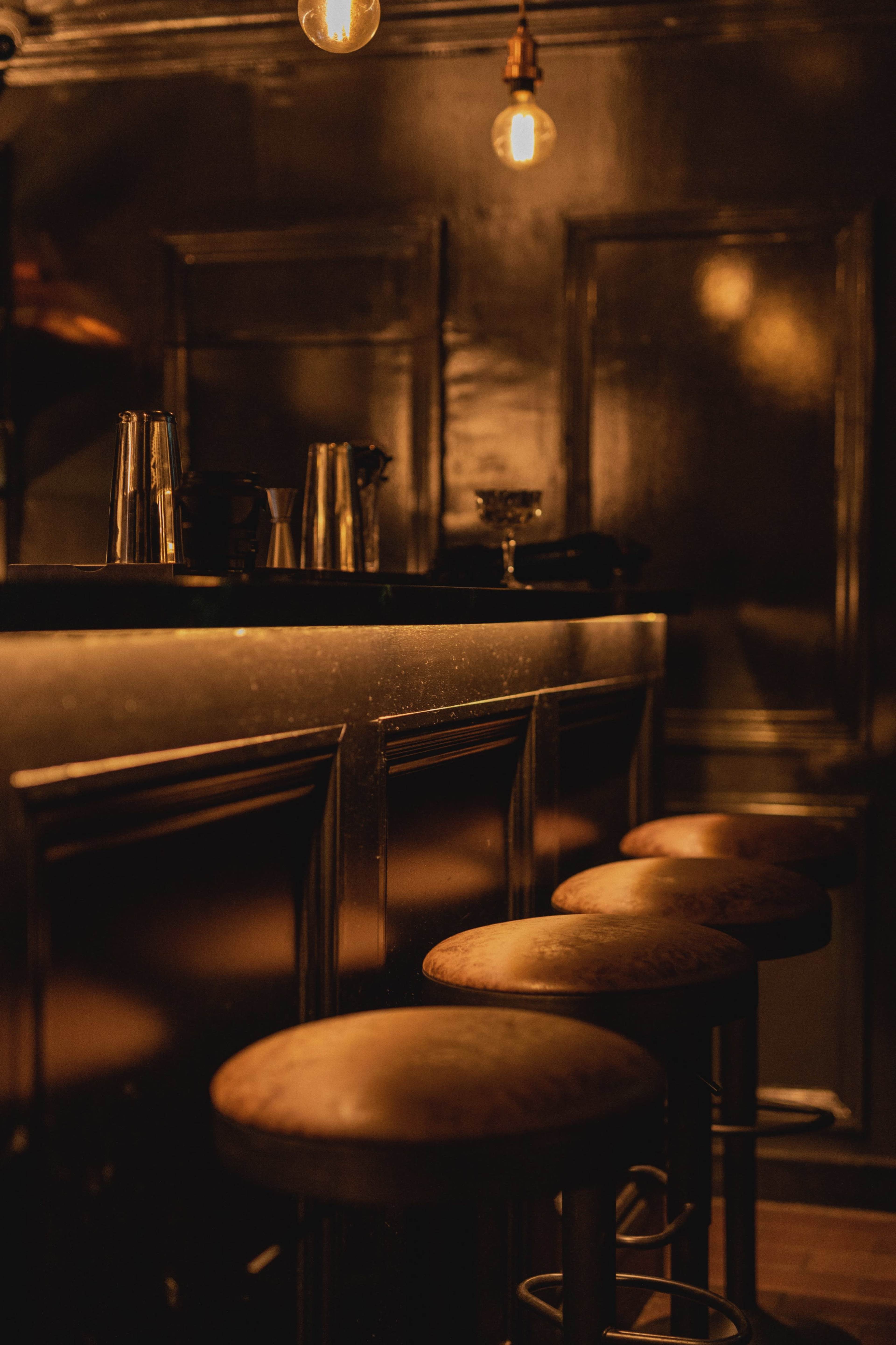 A dimly lit bar with wooden stools arranged in front of a polished counter.