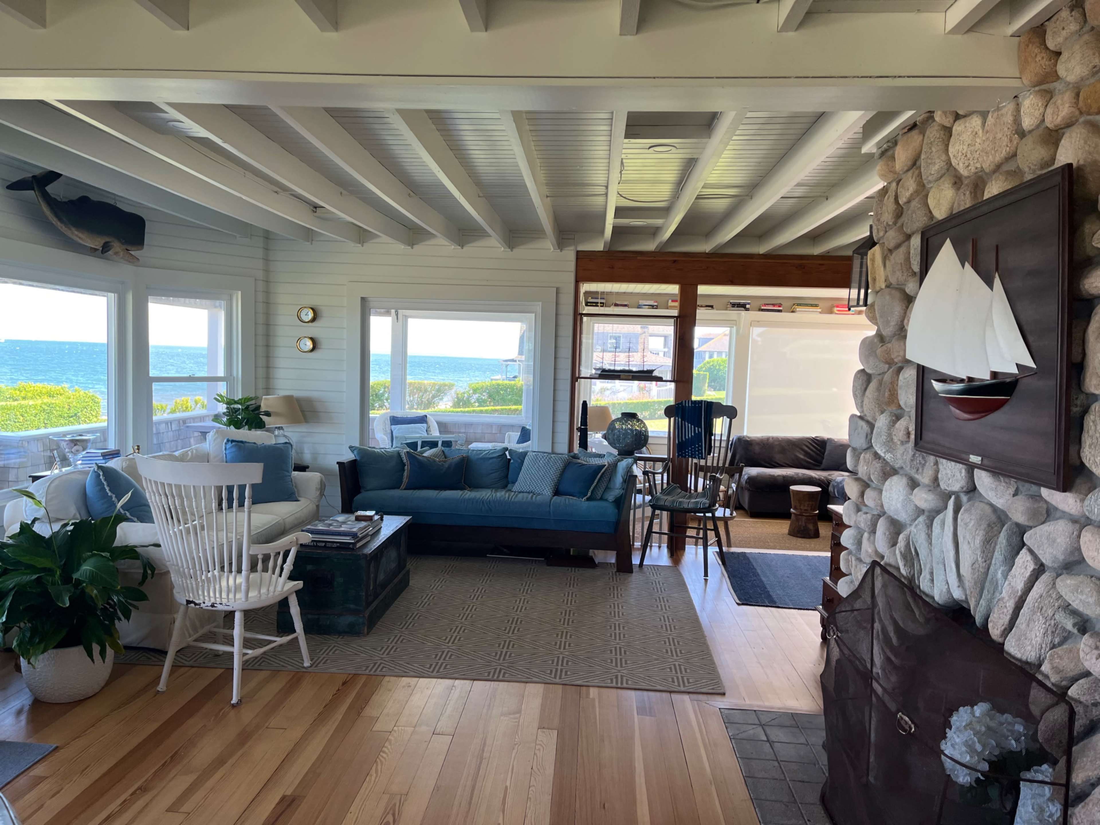 A bright and airy living room with a stone fireplace, large windows facing the ocean, and a mix of seating areas.