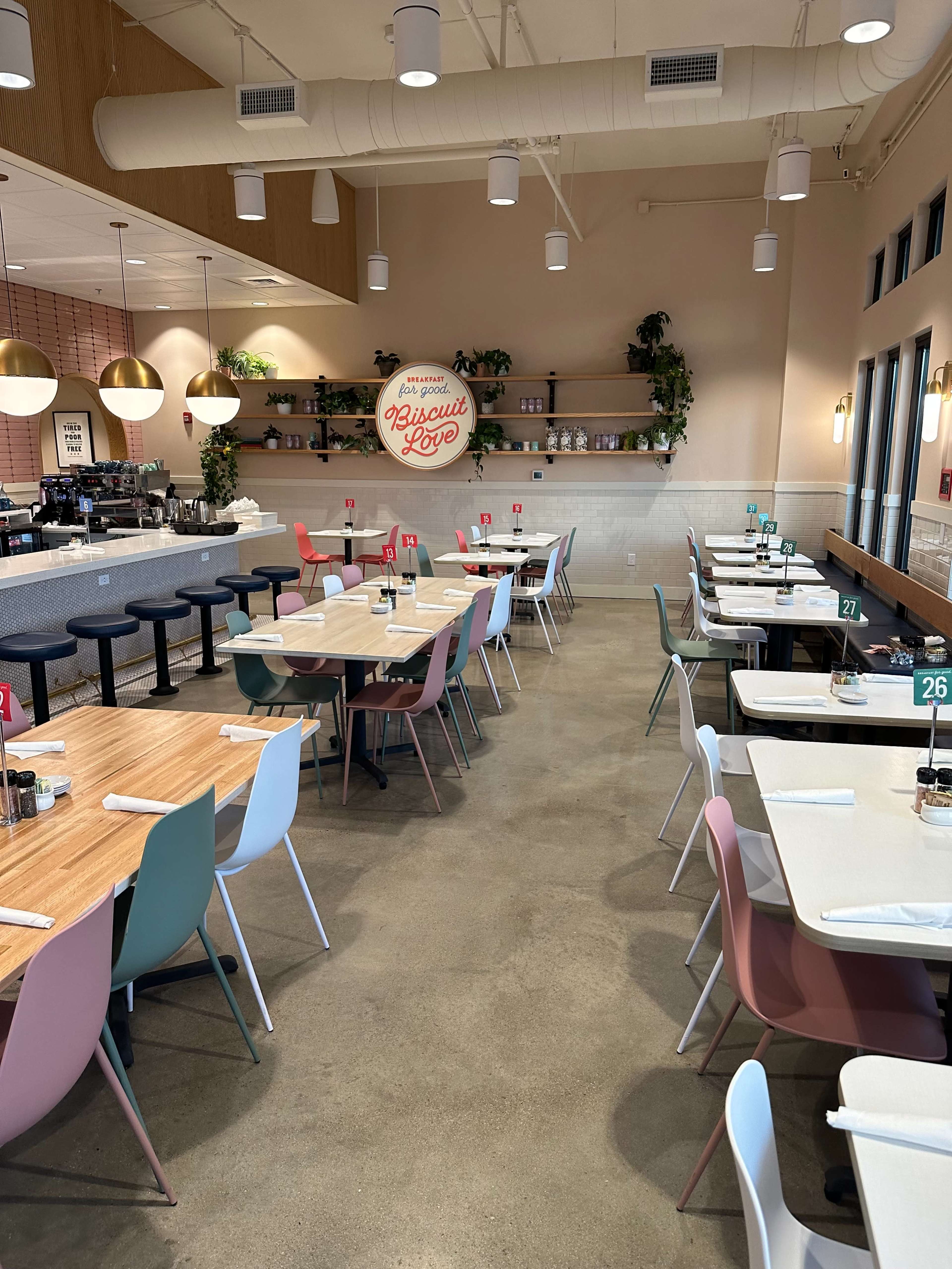 The image shows a spacious restaurant interior with colorful chairs, wooden tables, and a prominently displayed sign that reads "Biscuit Love."