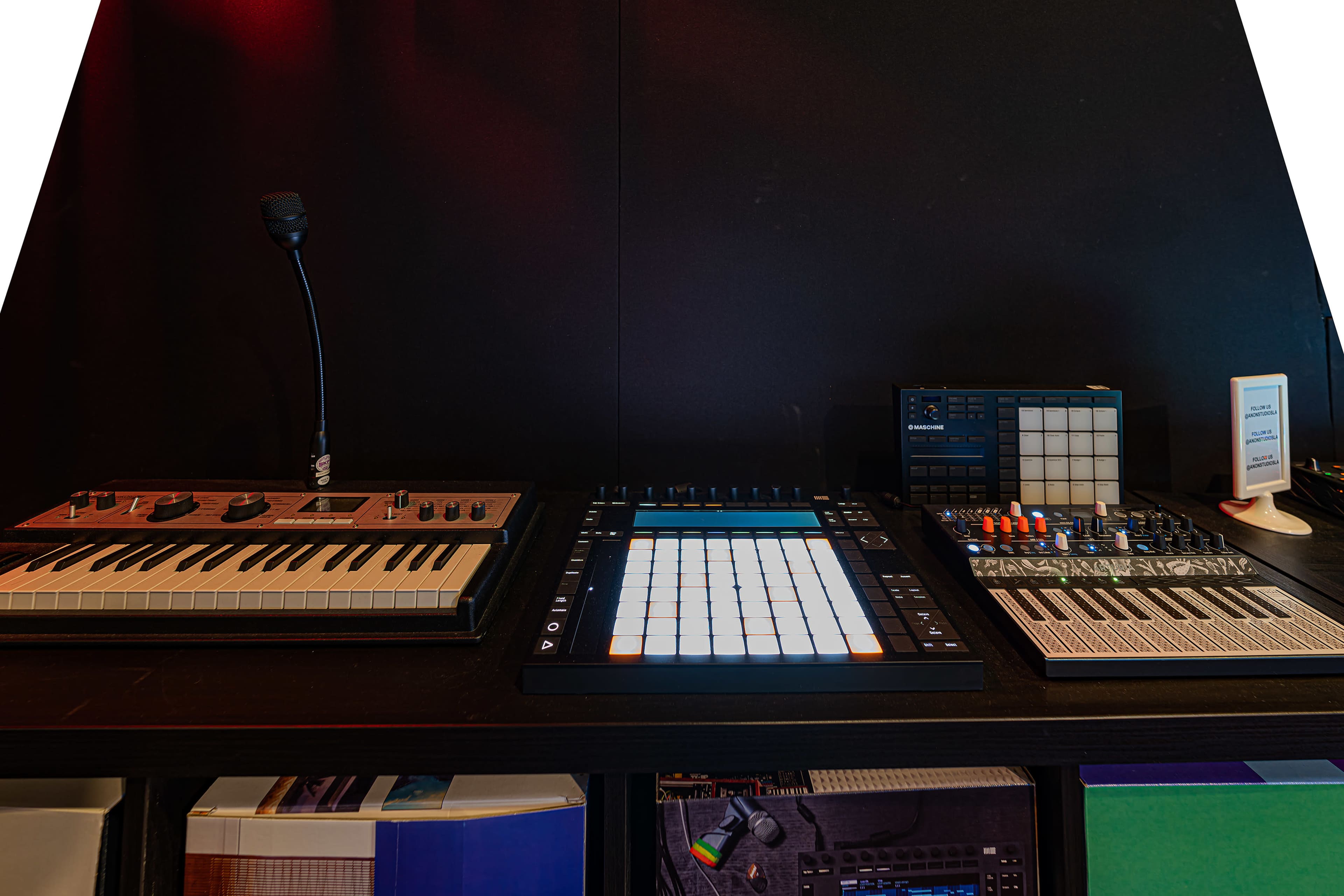 A music production setup featuring a keyboard, a MIDI controller with pads, and a small digital mixer on a black desk.