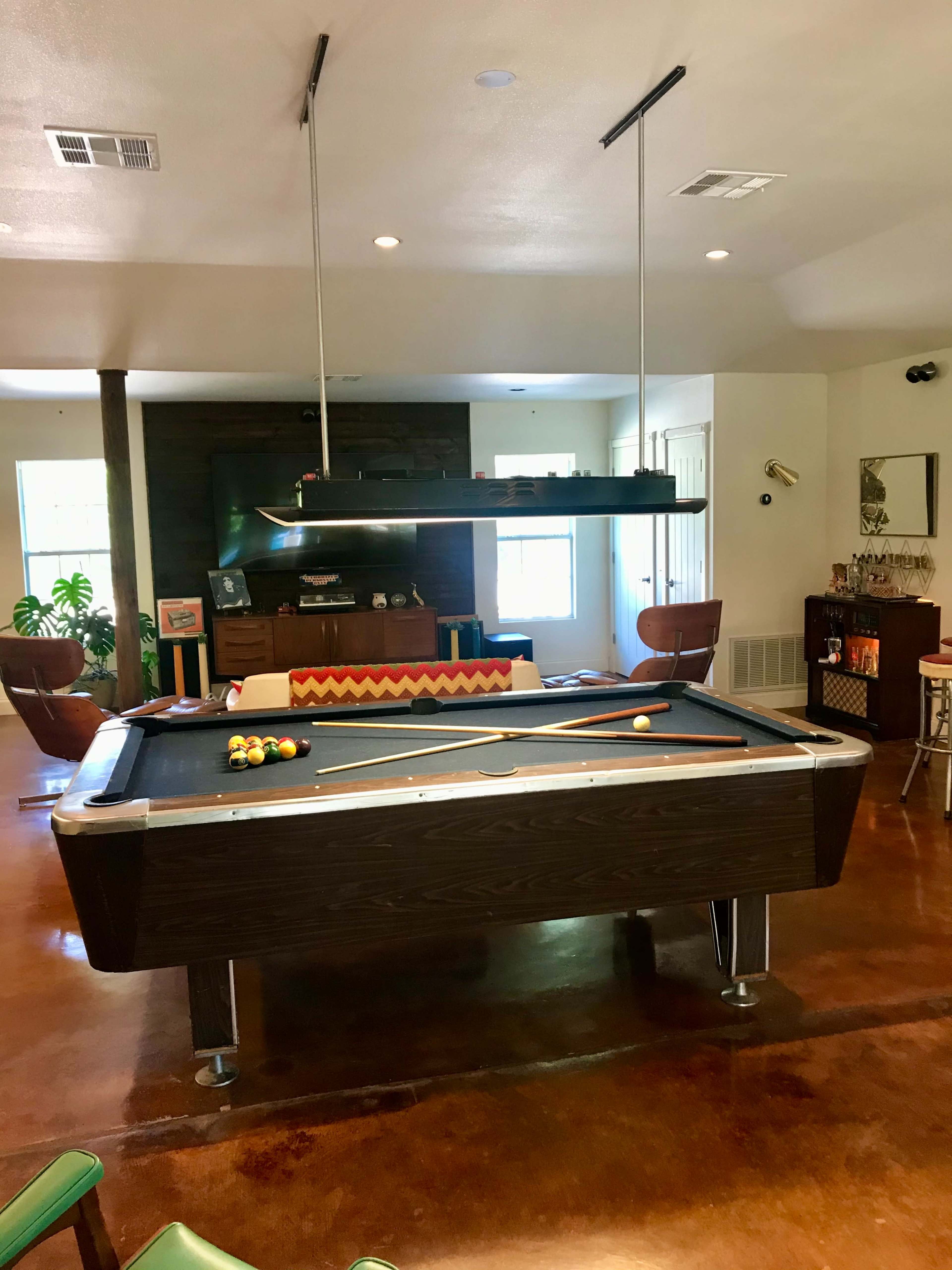 A game room featuring a pool table, a rack of pool balls, and comfortable seating arranged around the space.