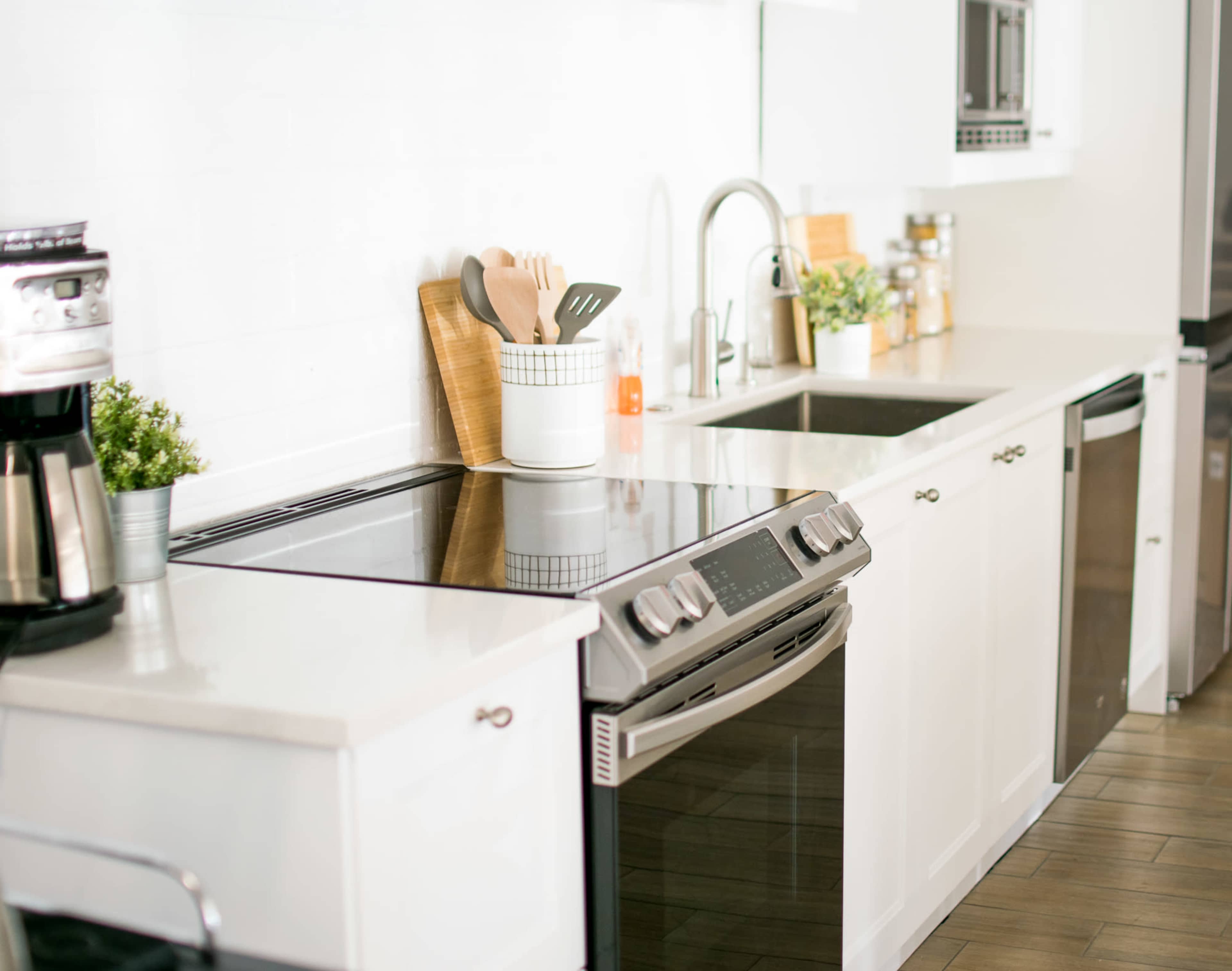 A modern kitchen with a sleek countertop, a stainless steel stove, and organized utensils in a container next to a sink.