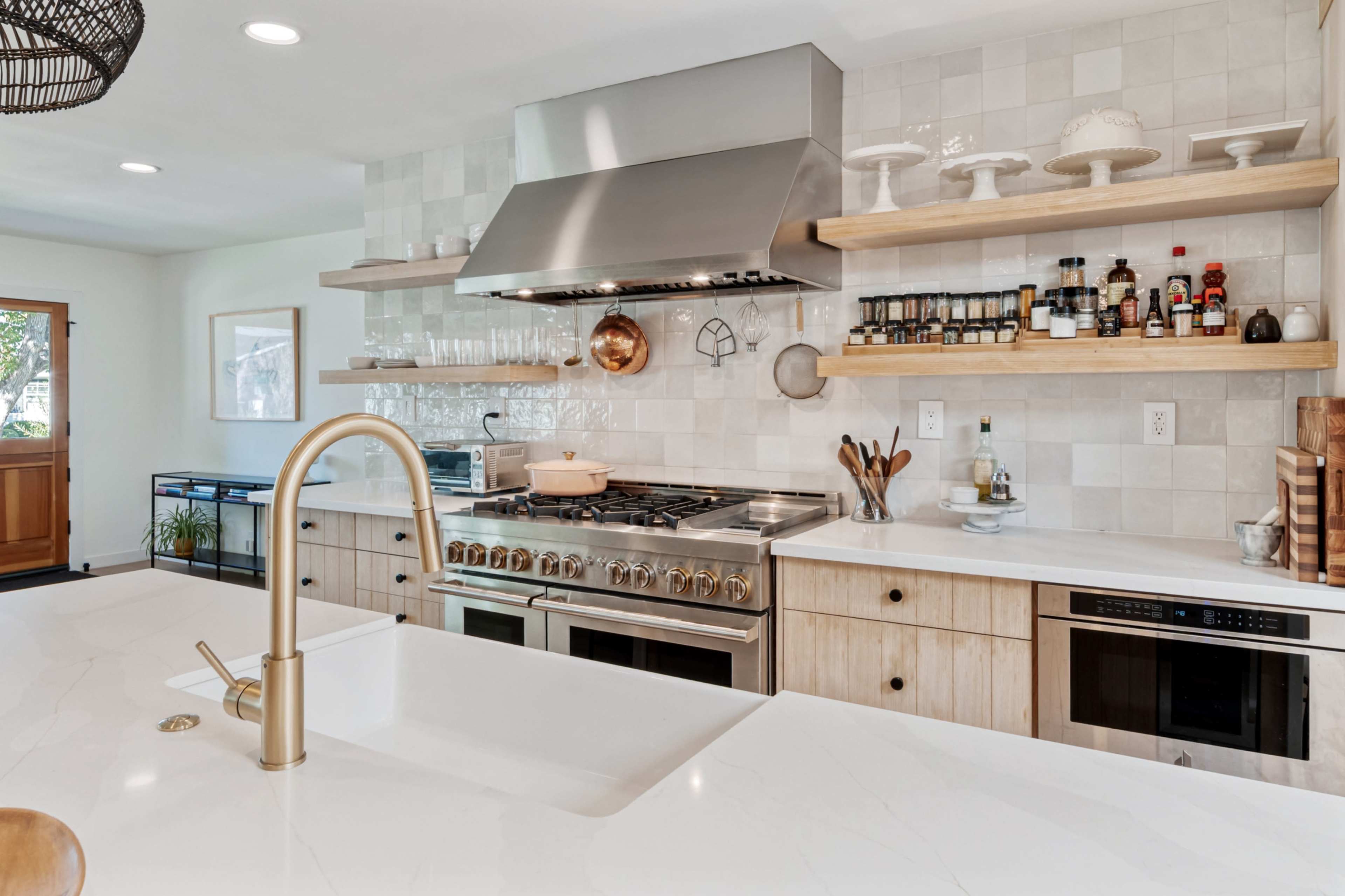 The image features a modern kitchen with stainless steel appliances, wooden shelves, and a large island with a sink.