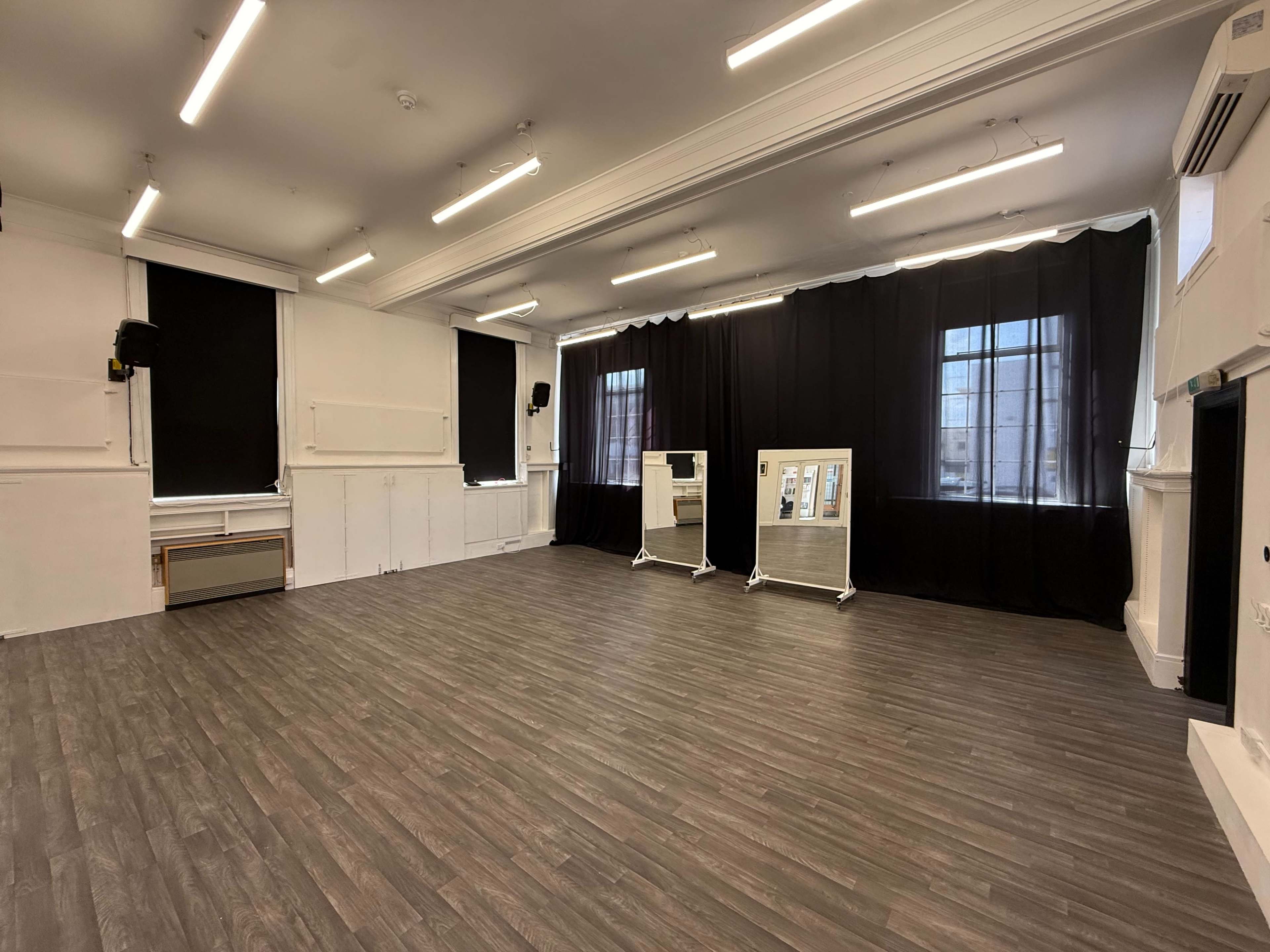 The image shows an empty, well-lit studio space with a wooden floor, black curtains blocking windows, and two display boards on stands.