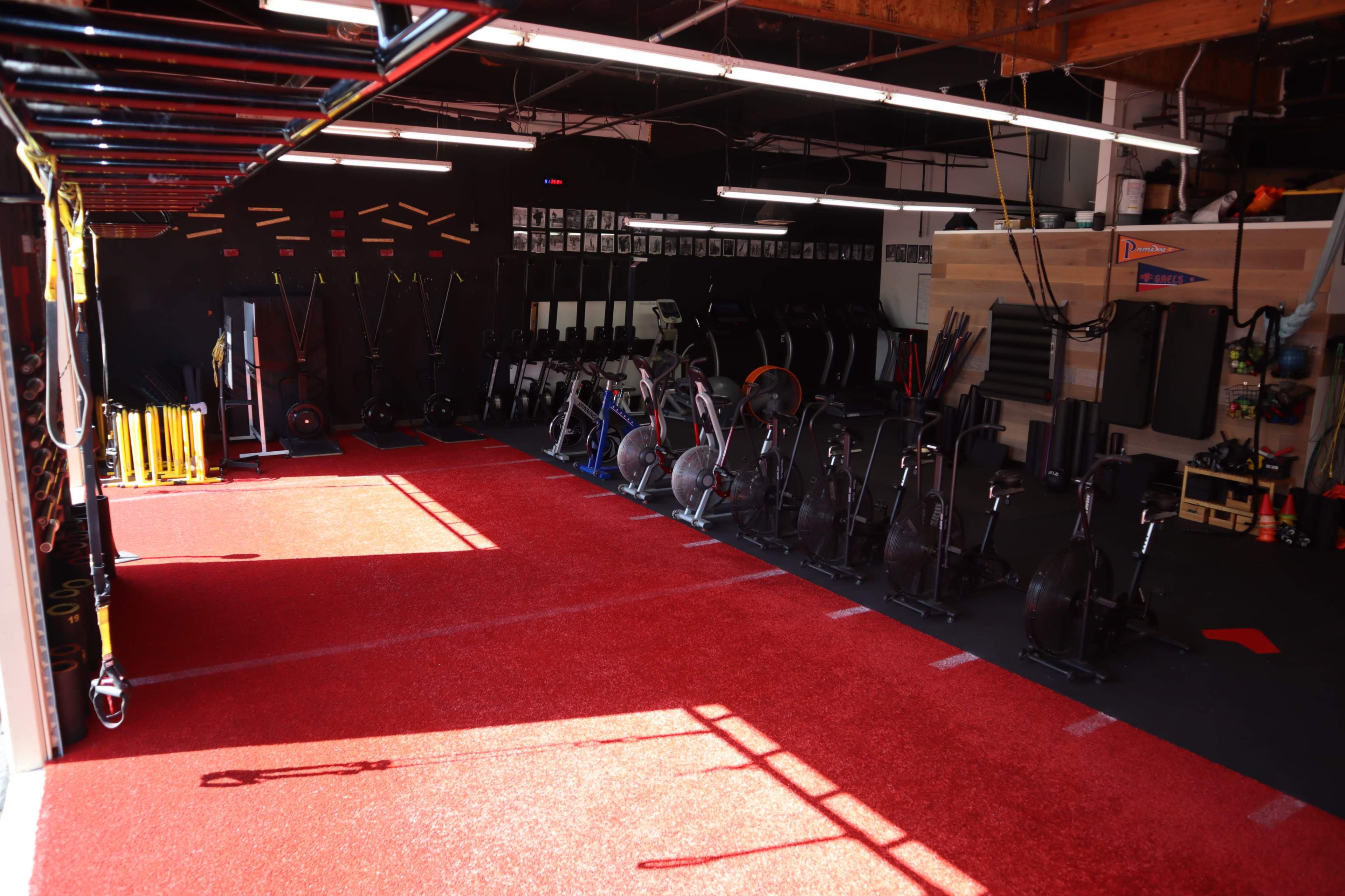 A fitness facility with rows of exercise equipment on a rubberized floor, flanked by a section of red turf.