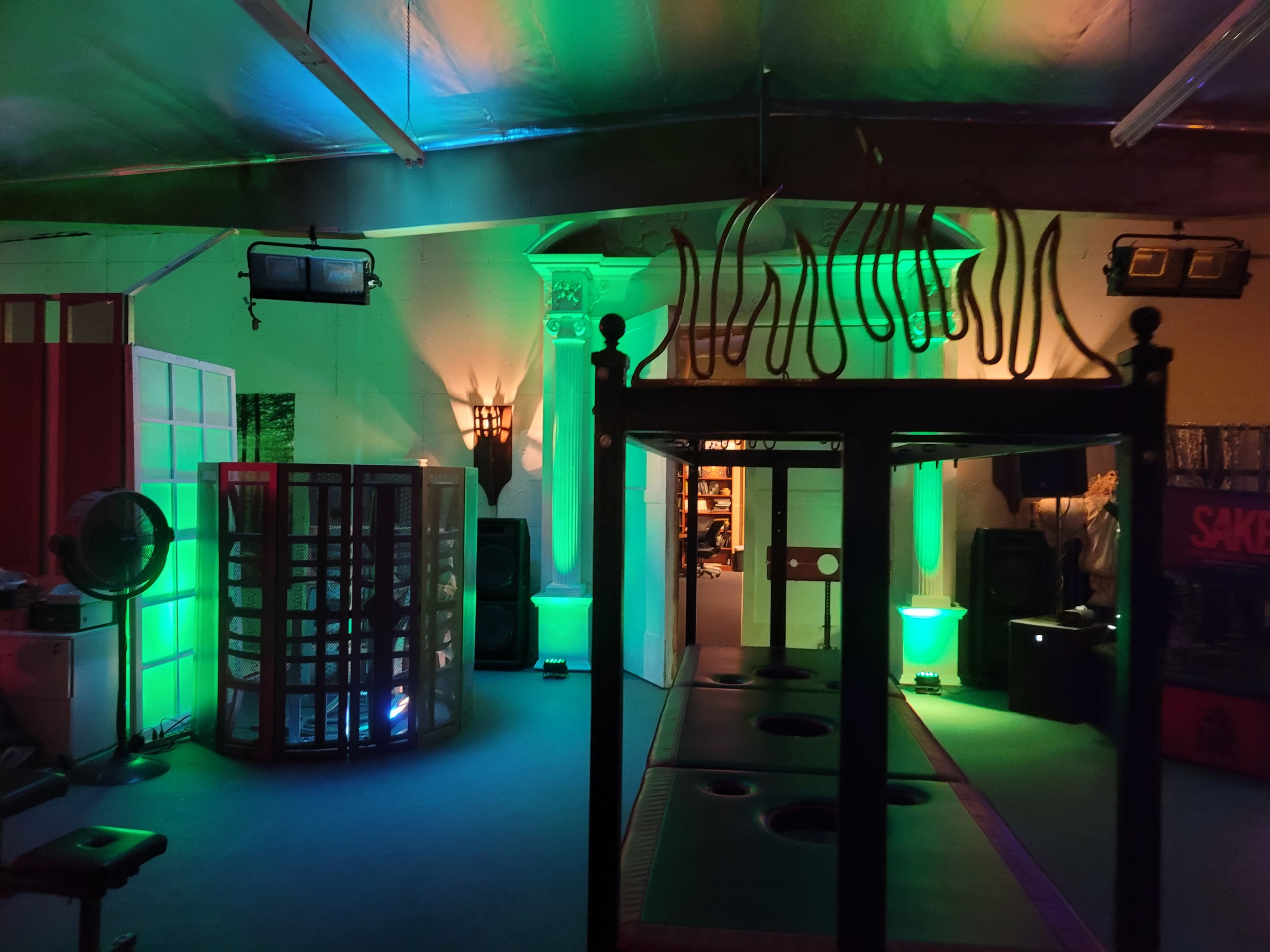 An indoor space with colorful lighting, featuring a central black structure and various illuminated objects and partitions.