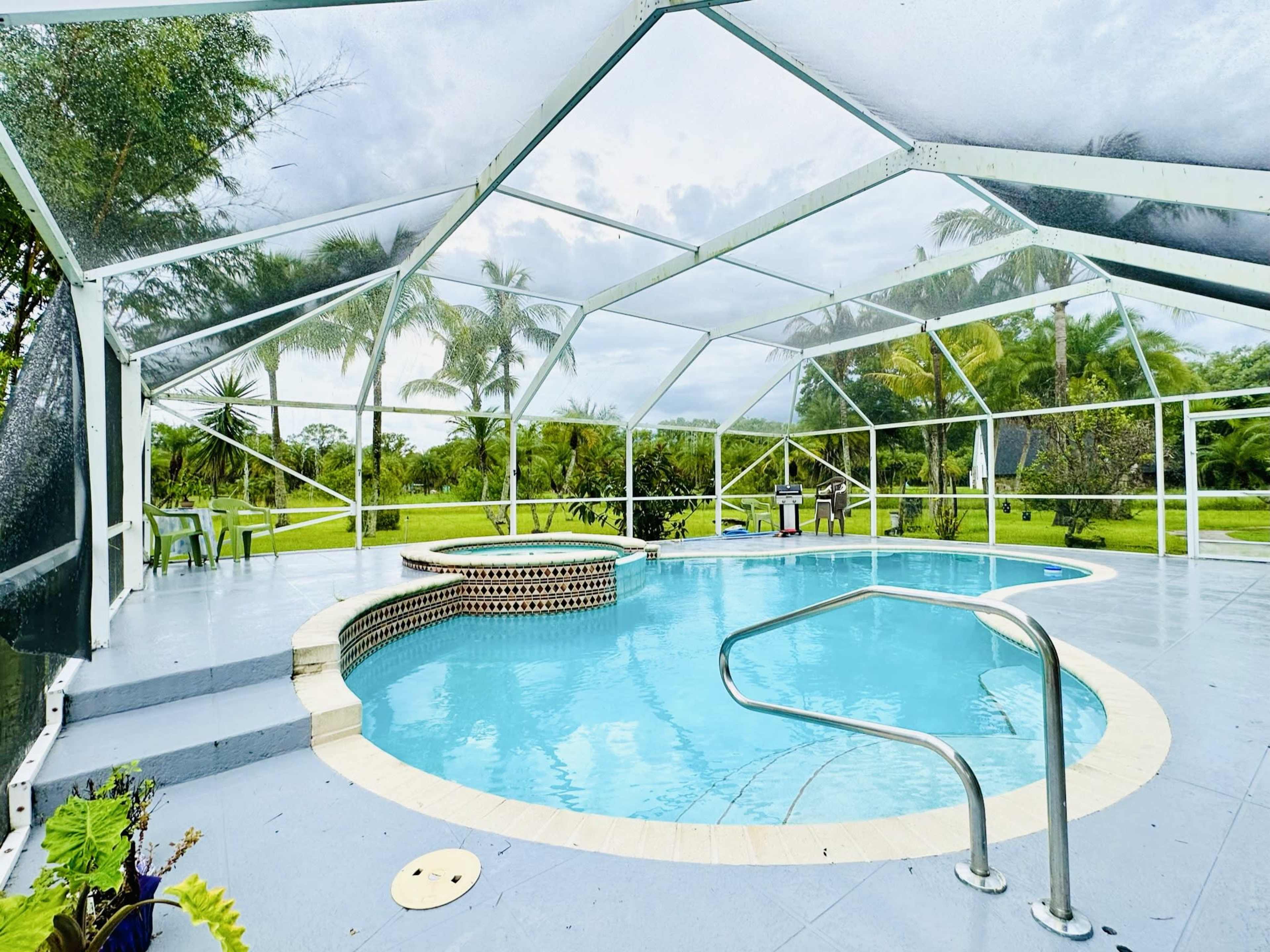 A screened-in outdoor pool area features a round hot tub, lounge chairs, and views of a green landscape.