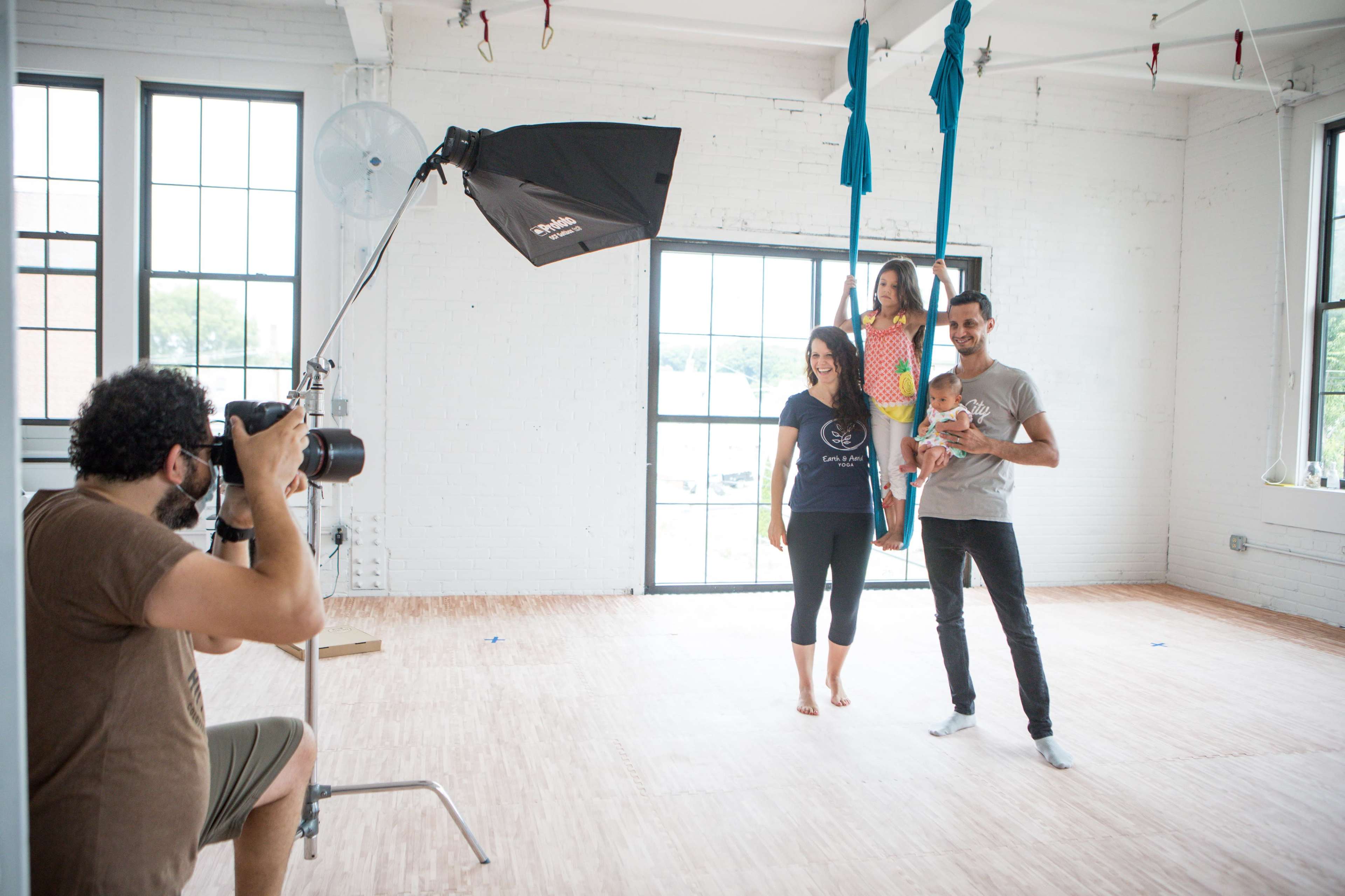 A photographer captures a family posing in a bright studio with aerial silks.