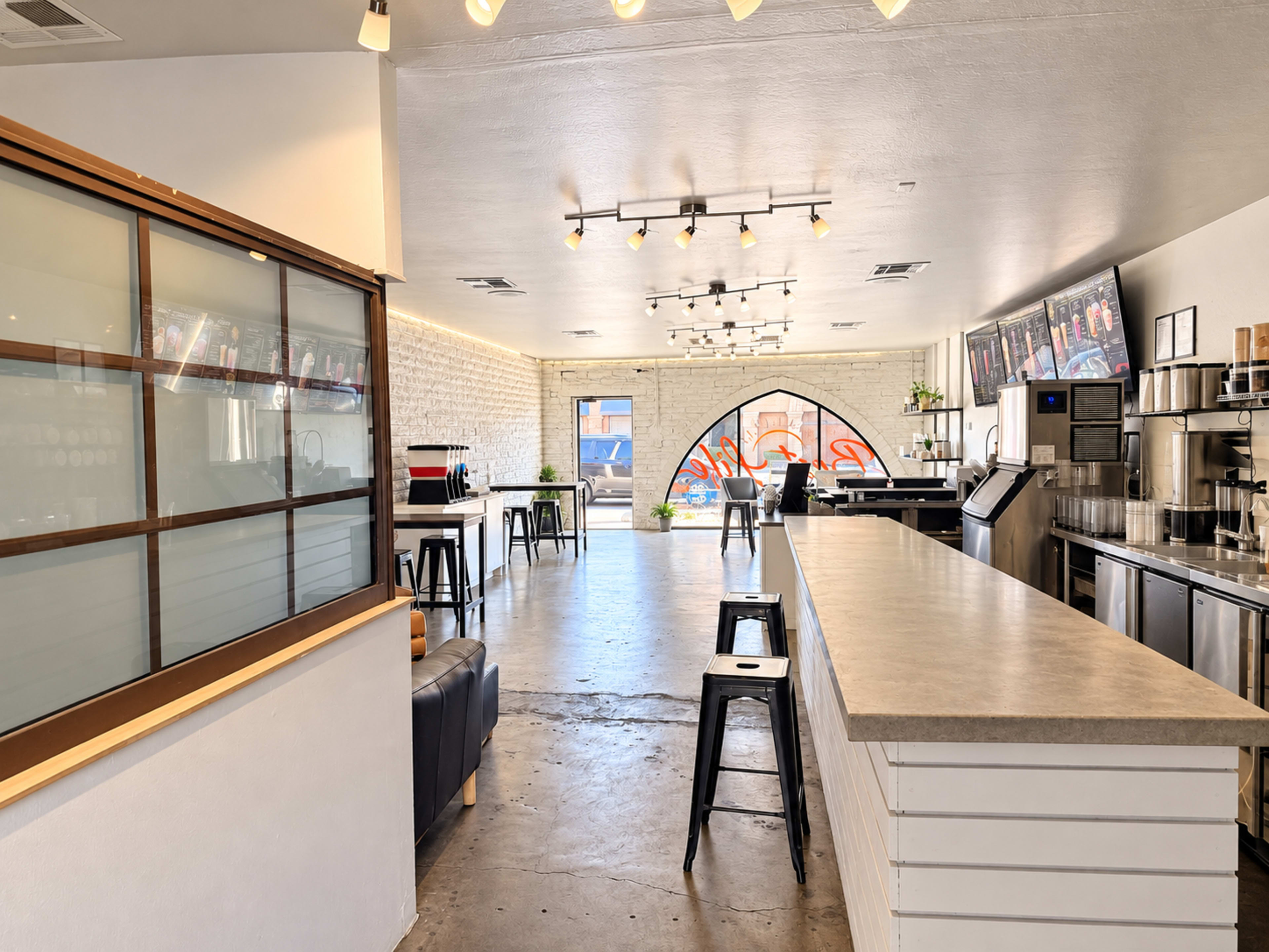 The image shows a modern cafe interior with a long counter, seating area, and large windows providing natural light.