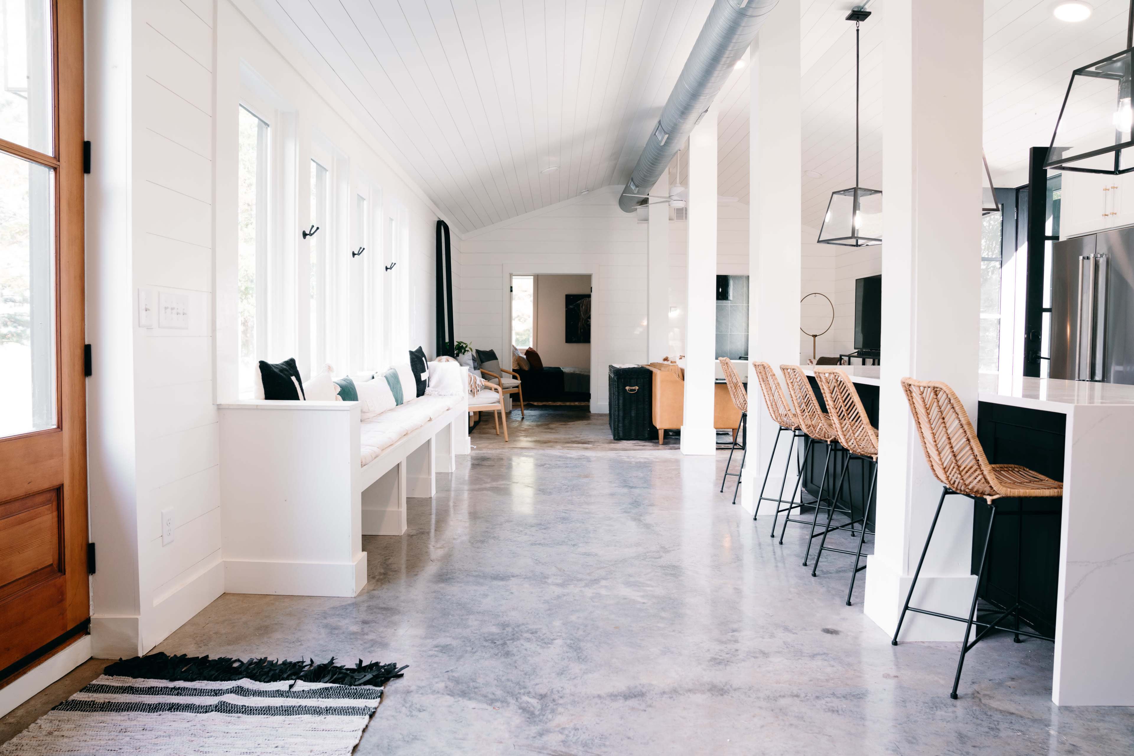 A modern interior space featuring a kitchen with bar stools, a dining area, and large windows allowing natural light to fill the room.
