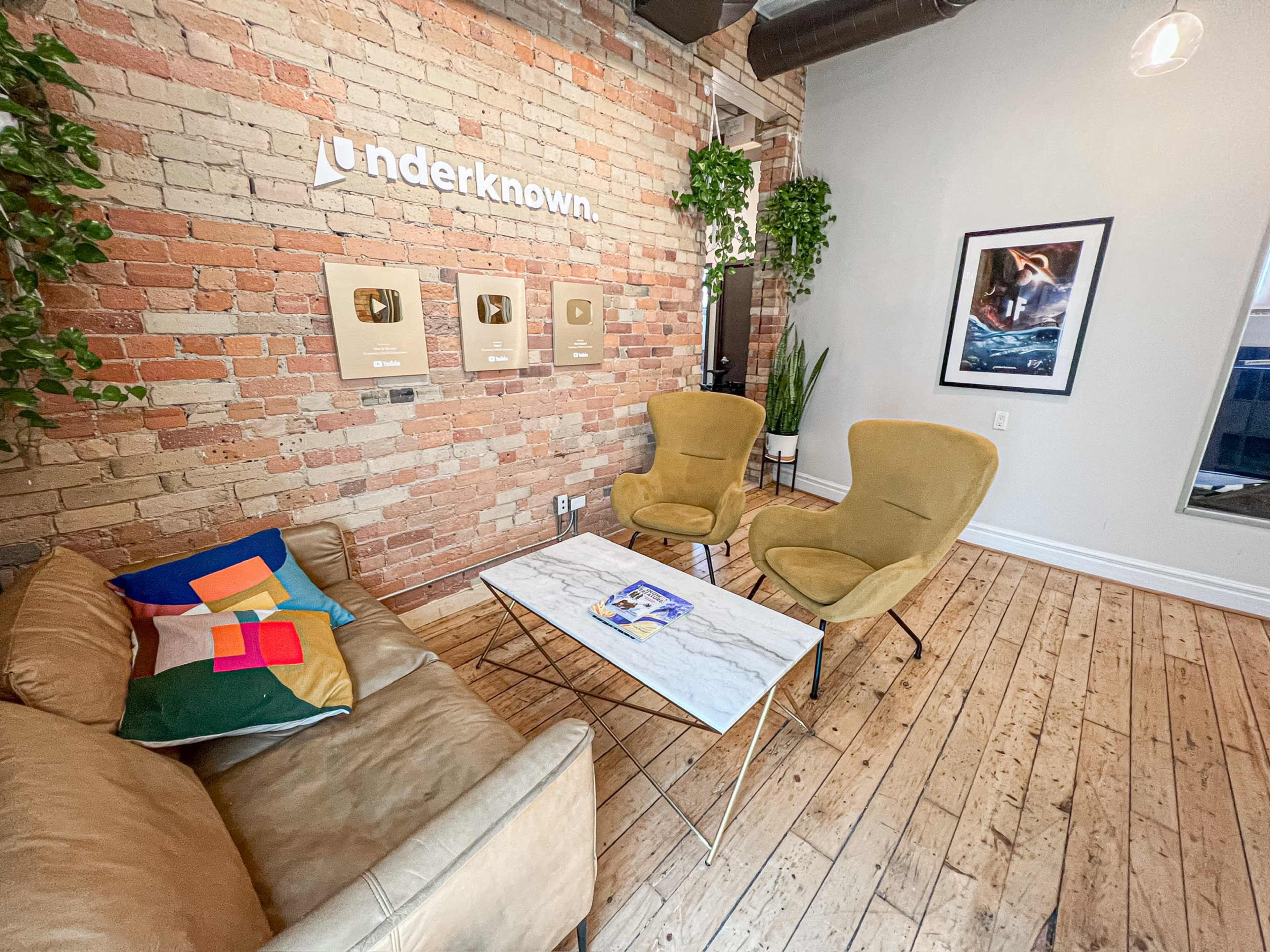 A modern lounge area with a brick wall, two armchairs, a couch, and a coffee table displaying framed awards.