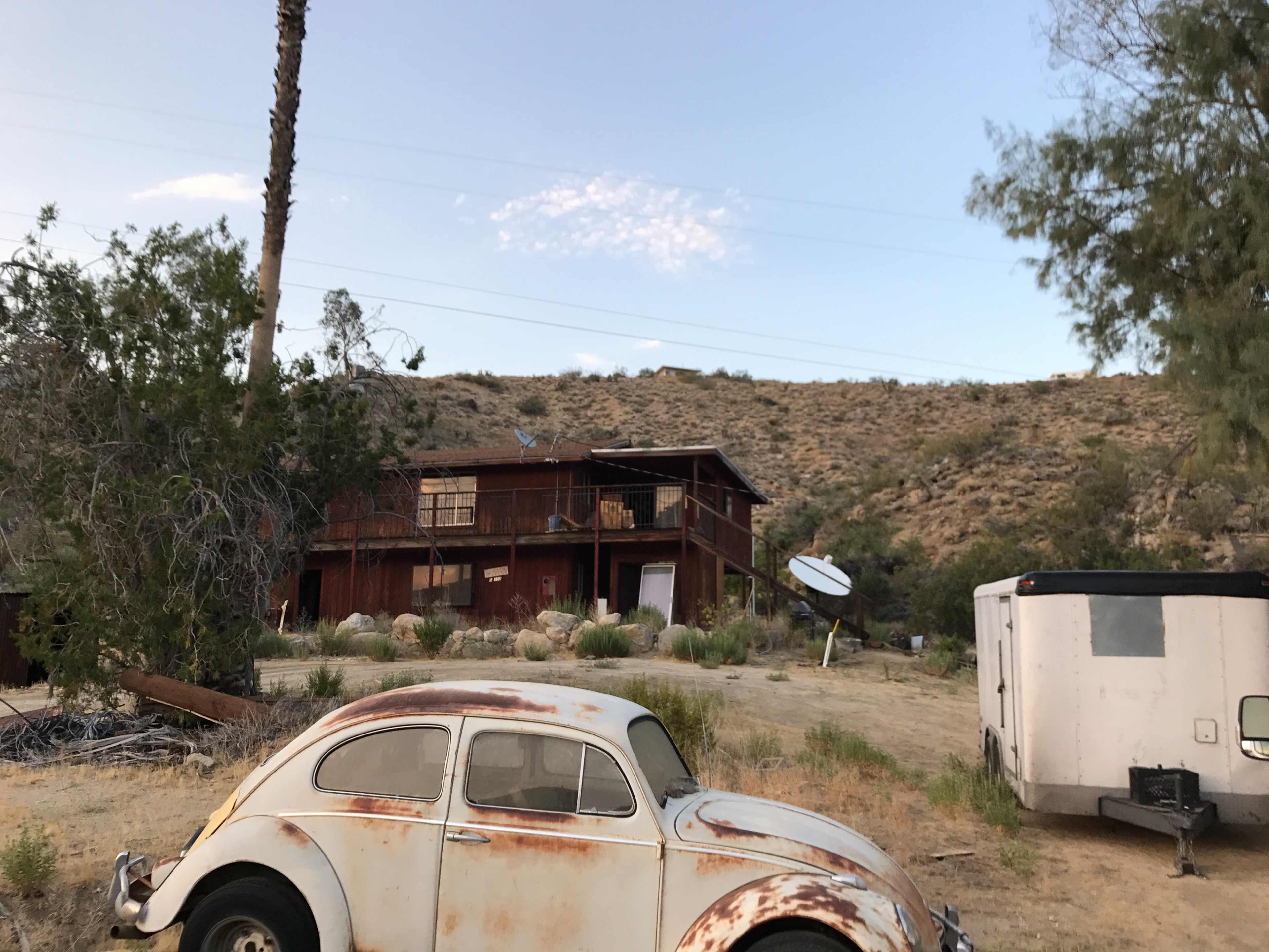 A weathered red building sits on a hillside, accompanied by a rusty Volkswagen Beetle in the foreground.