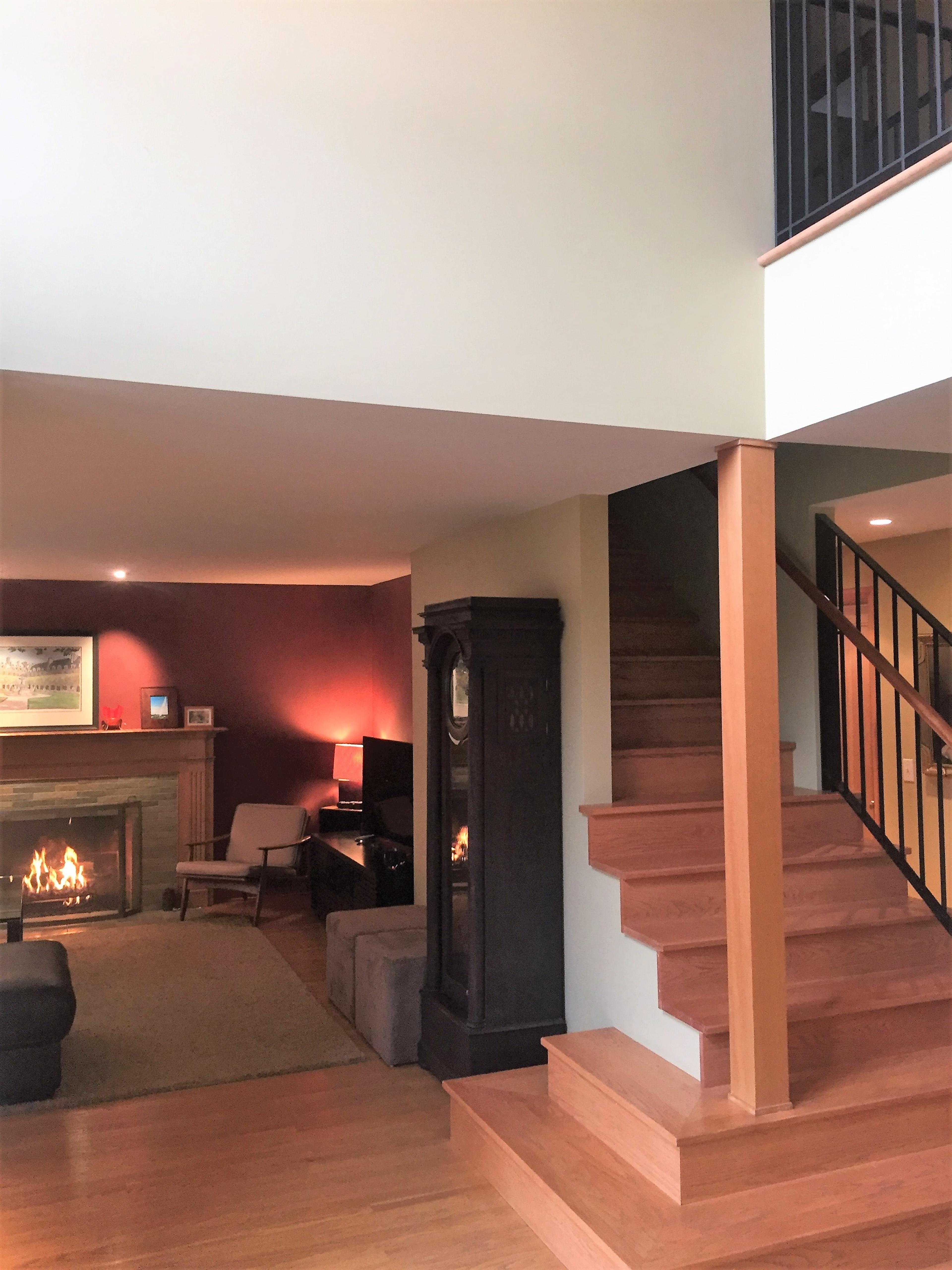 A modern living room with a staircase leading to an upper level, featuring a cozy fireplace and a large wall-mounted television.
