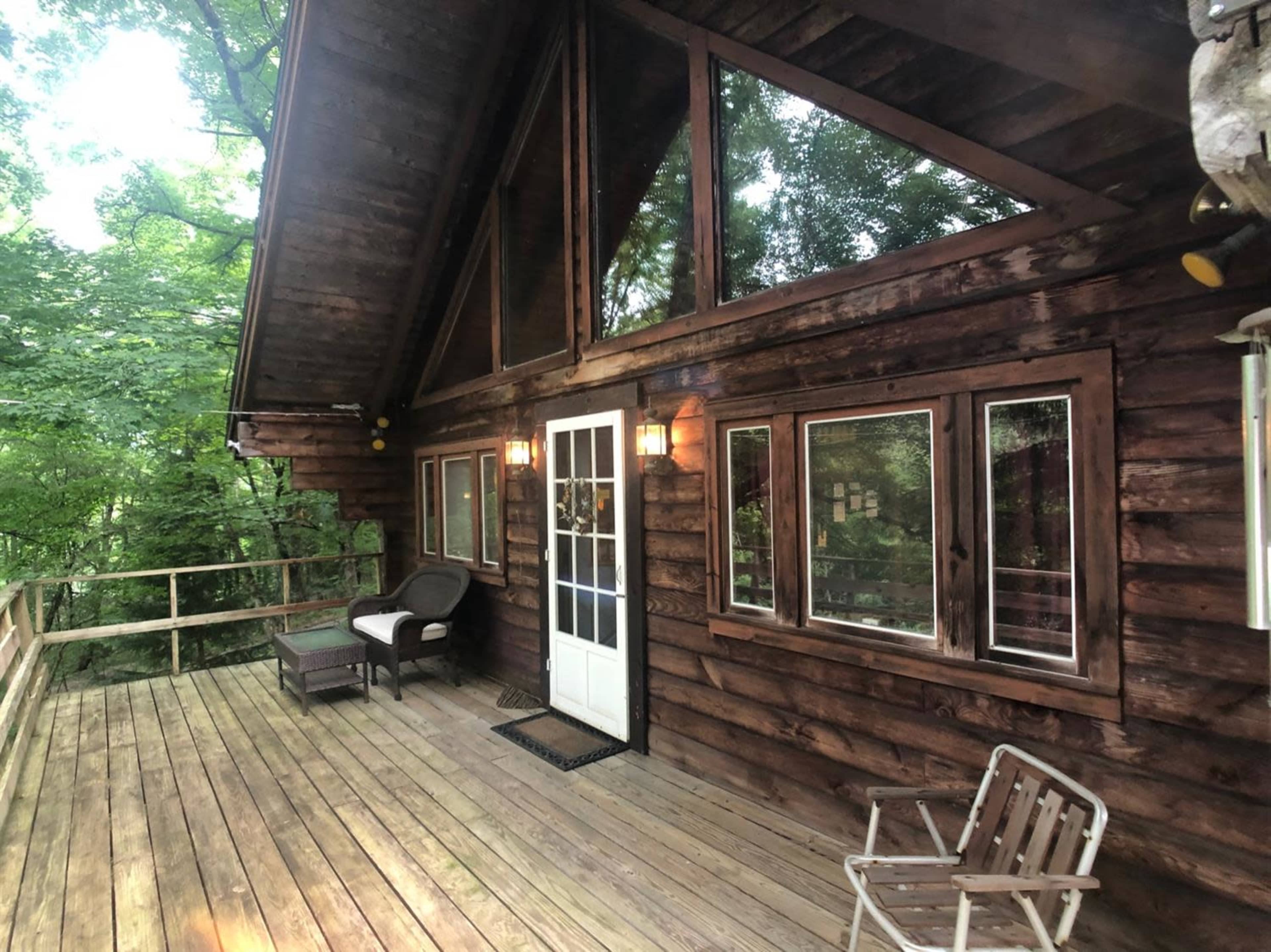 A rustic wooden cabin with large windows and a porch overlooking a forested area.