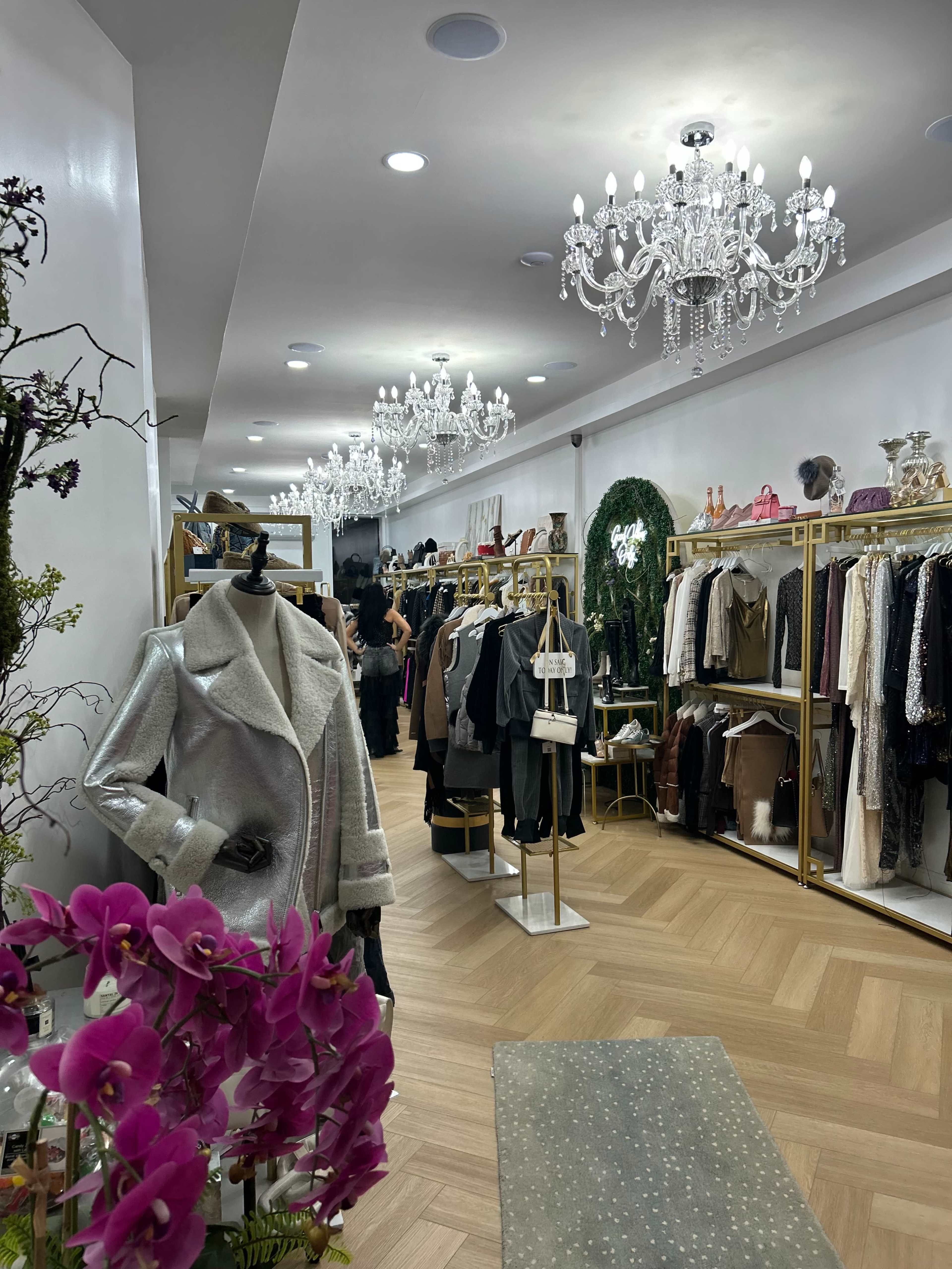 The interior of a clothing boutique features elegant chandeliers, clothing racks filled with various garments, and decorative floral arrangements.