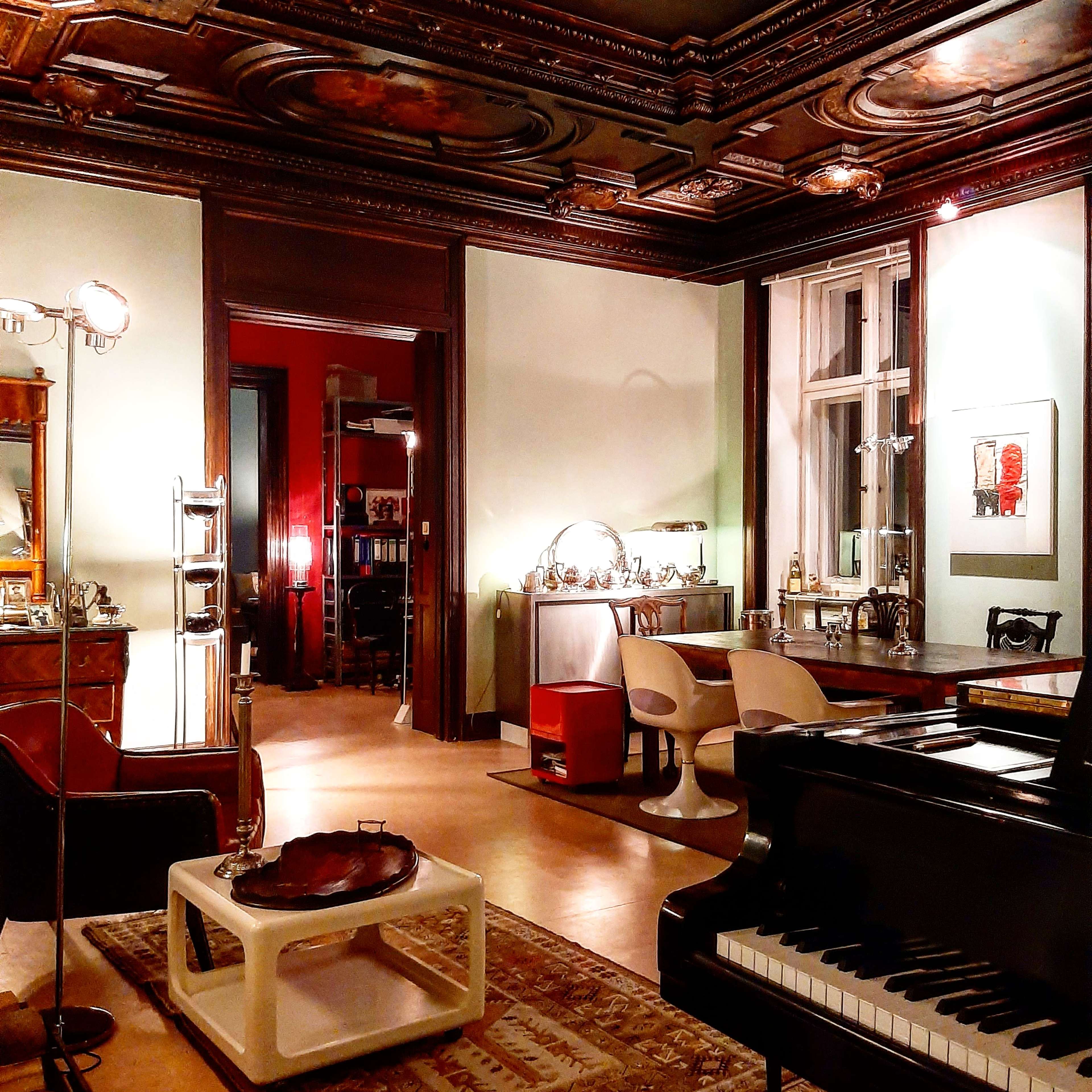 A stylish room featuring a grand piano, modern furniture, and dark wood accents, with a view into an adjacent space.