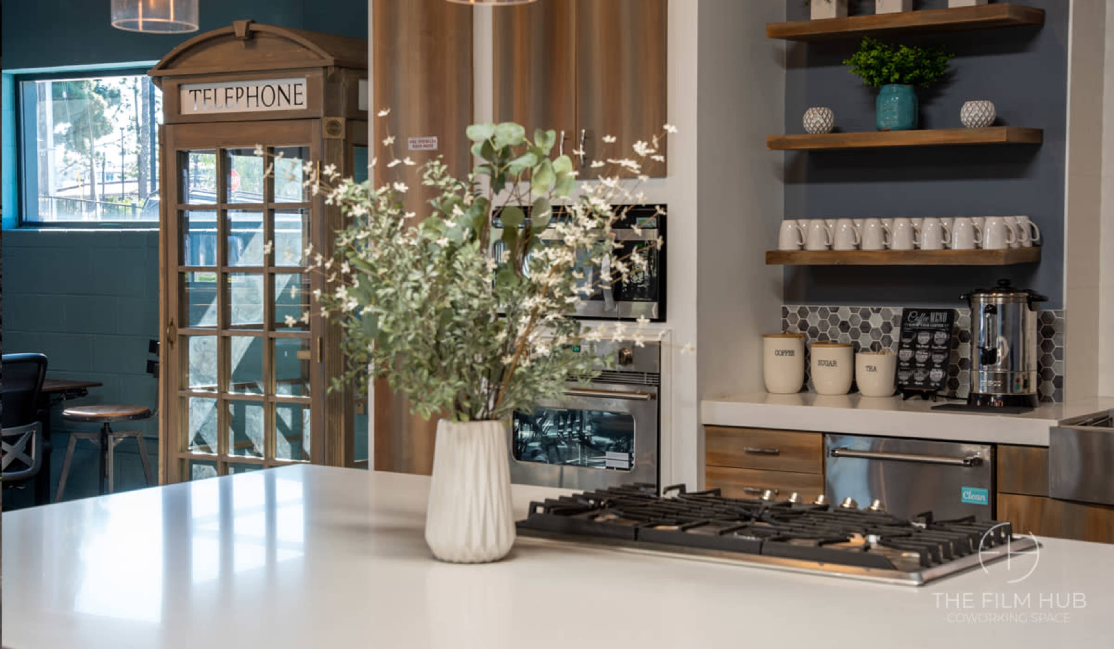 A modern kitchen features a gas stove, a vase of flowers, and a vintage telephone booth in the background.