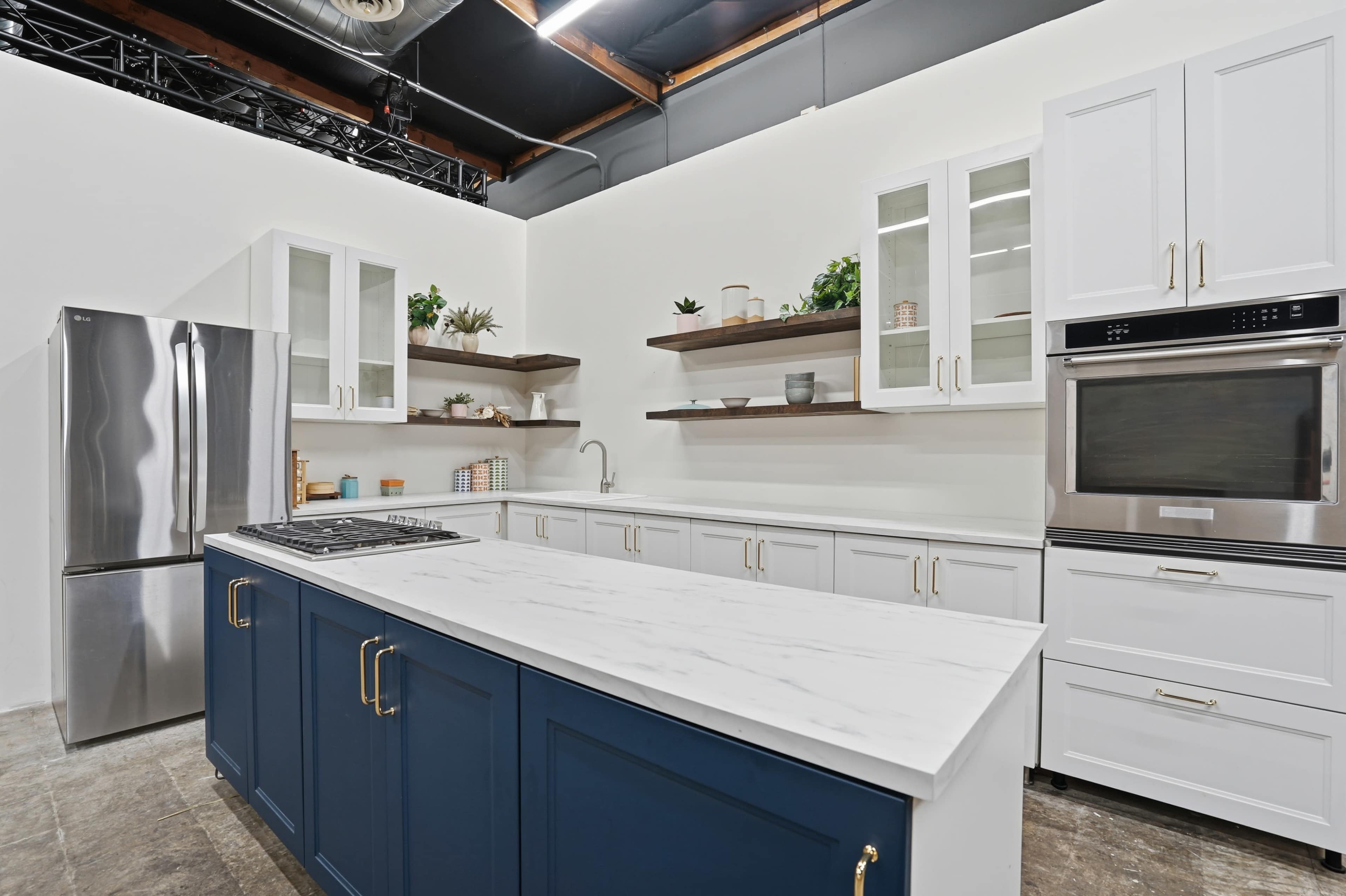 The image shows a modern kitchen with white cabinets, a blue island, stainless steel appliances, and open shelving.