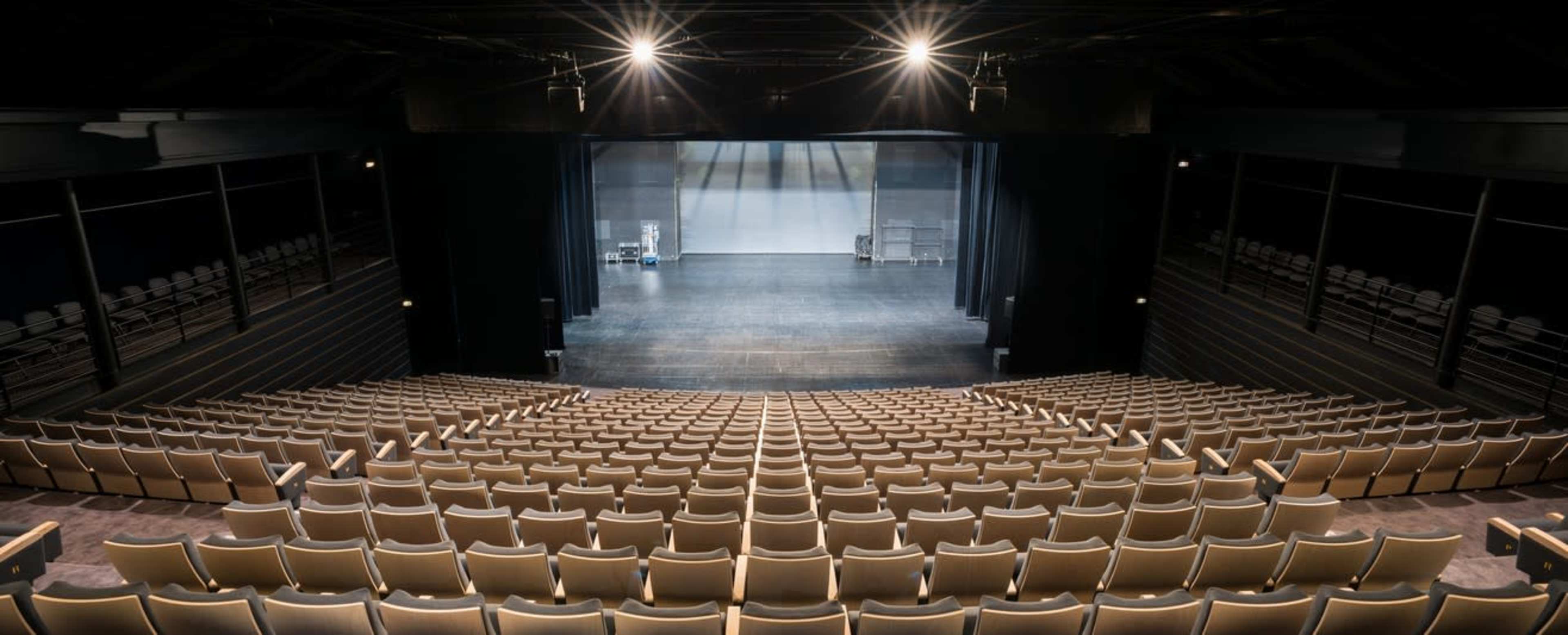 The image shows an empty theater with a wide seating area facing a dark stage.