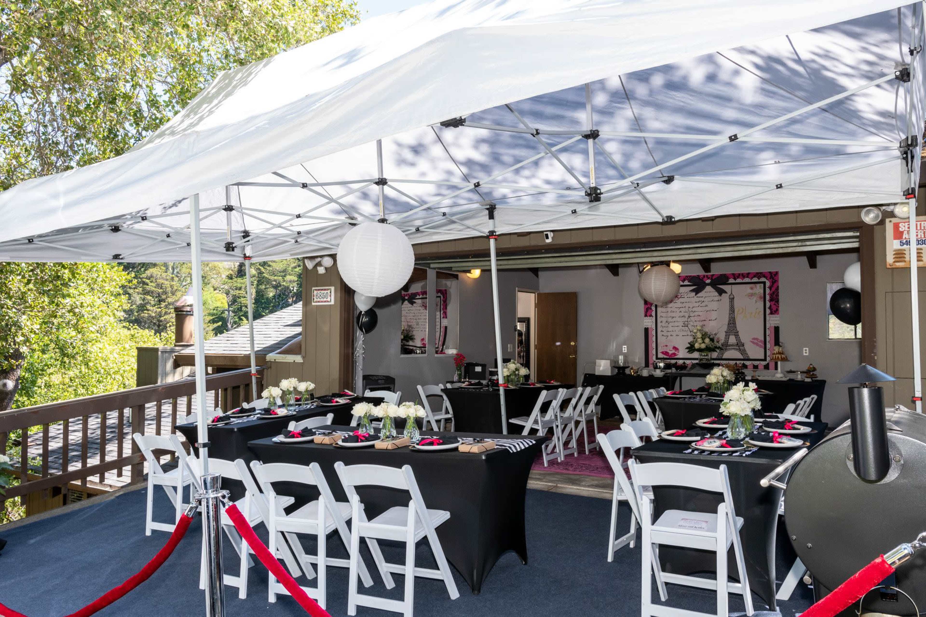 A tented outdoor event space features black table linens, floral centerpieces, and red carpet entrances.