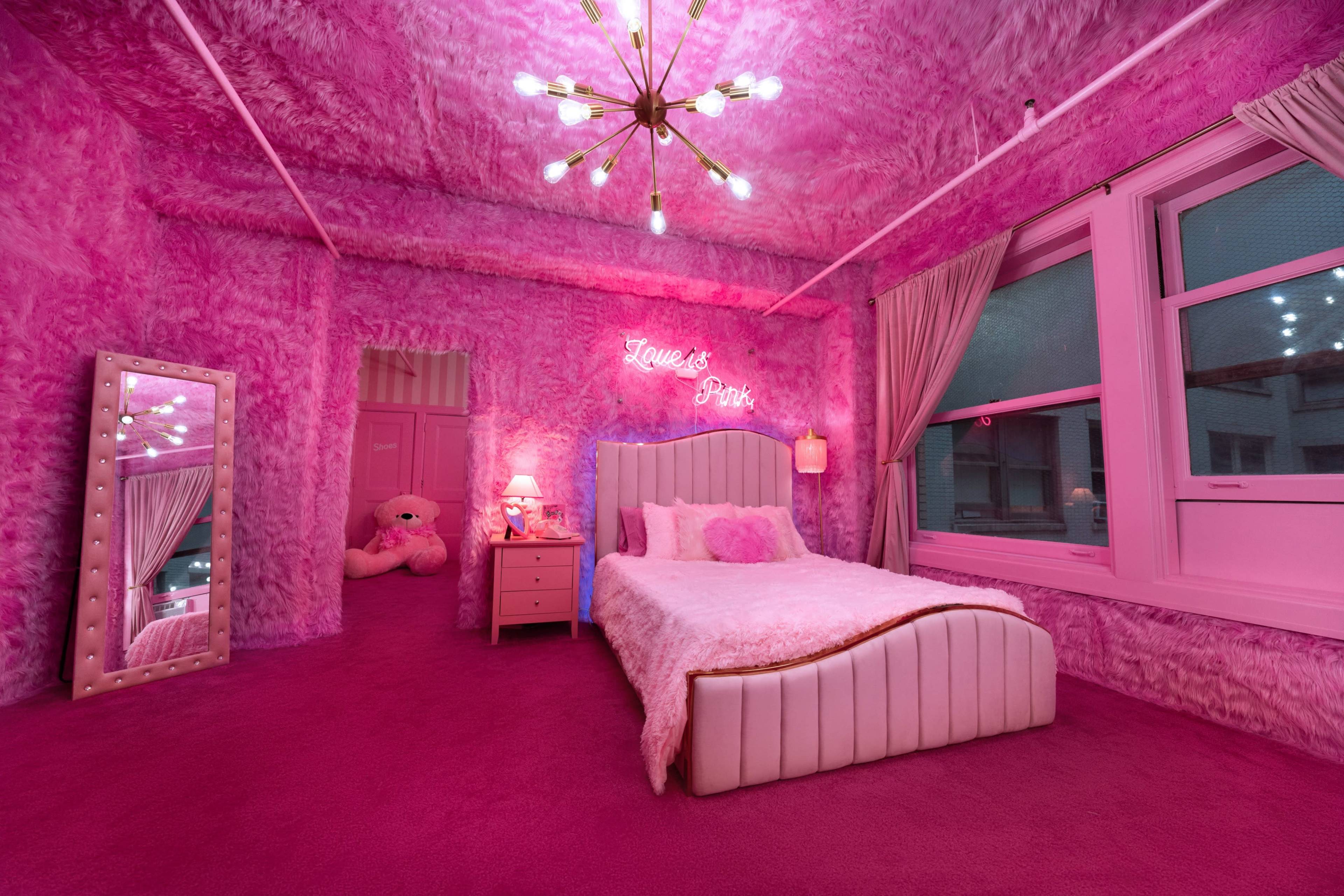 The room features pink walls and furnishings, with a plush bed, a glowing light fixture, and a large teddy bear in the corner.