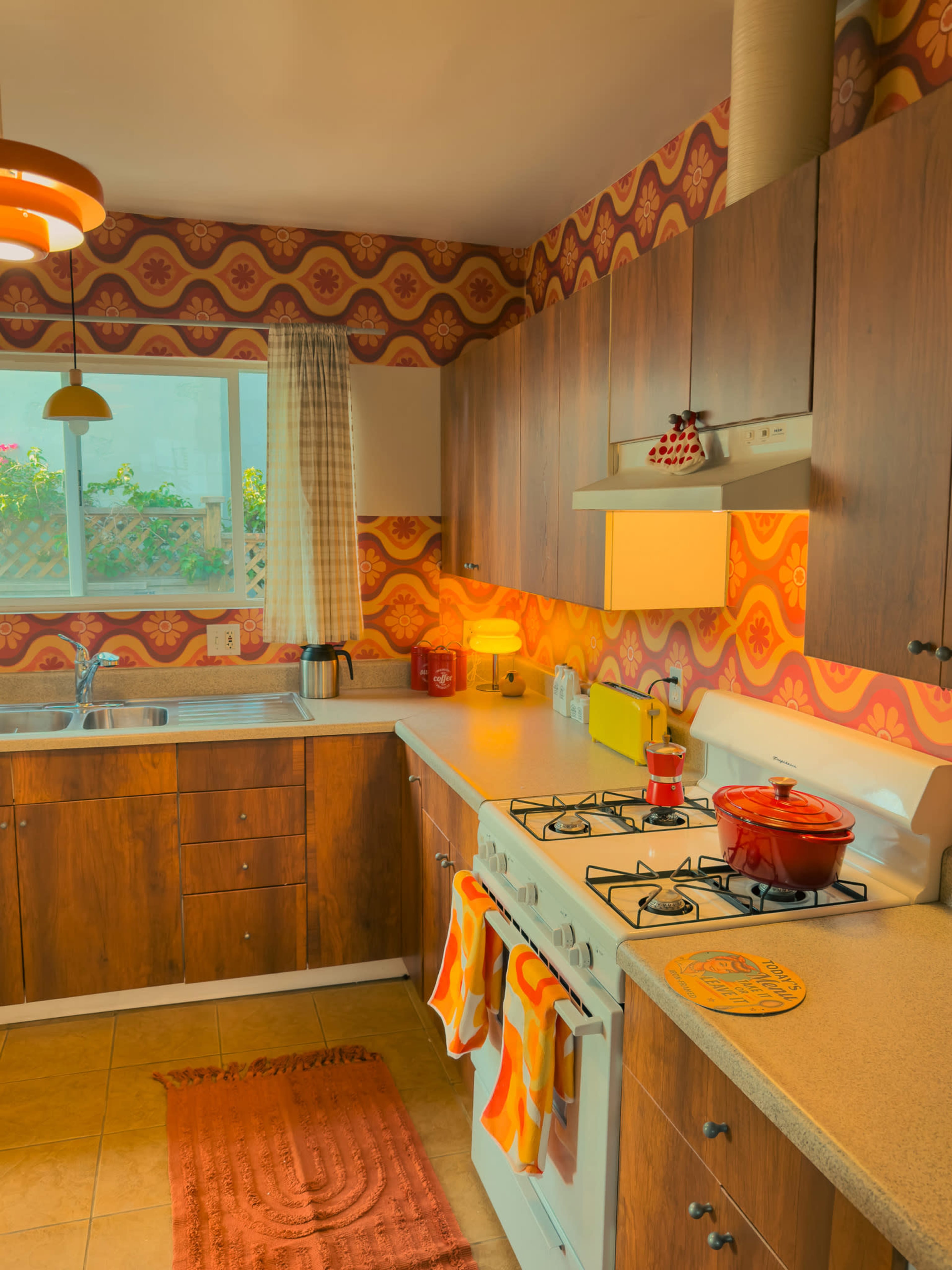 The kitchen features wooden cabinets, a gas stove, and retro wallpaper with a colorful pattern.