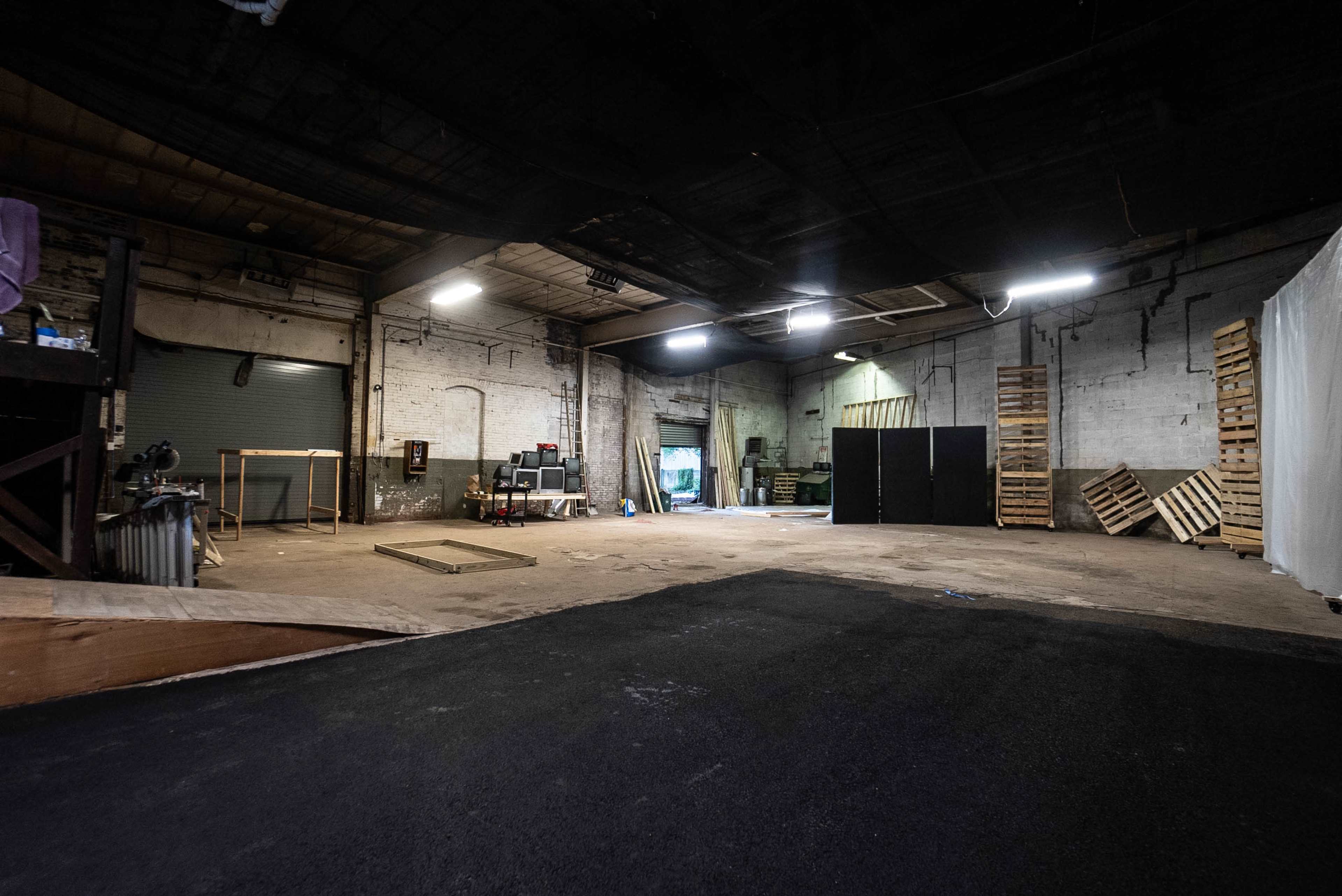 A large, empty industrial warehouse space with wooden pallets stacked against the walls and a loading bay visible at the far end.