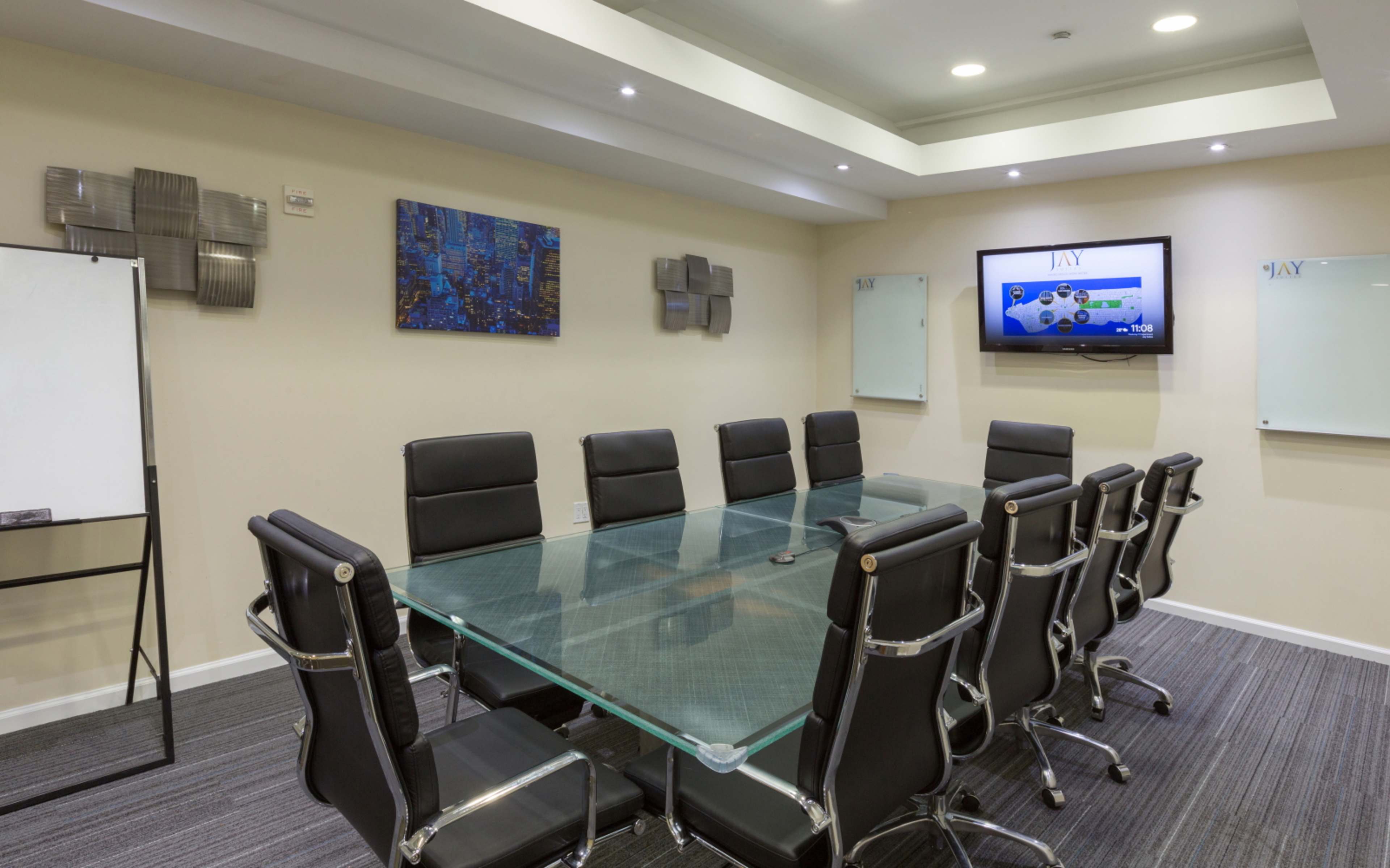 A modern conference room features a large glass table surrounded by black ergonomic chairs, with digital displays and whiteboards on the walls.