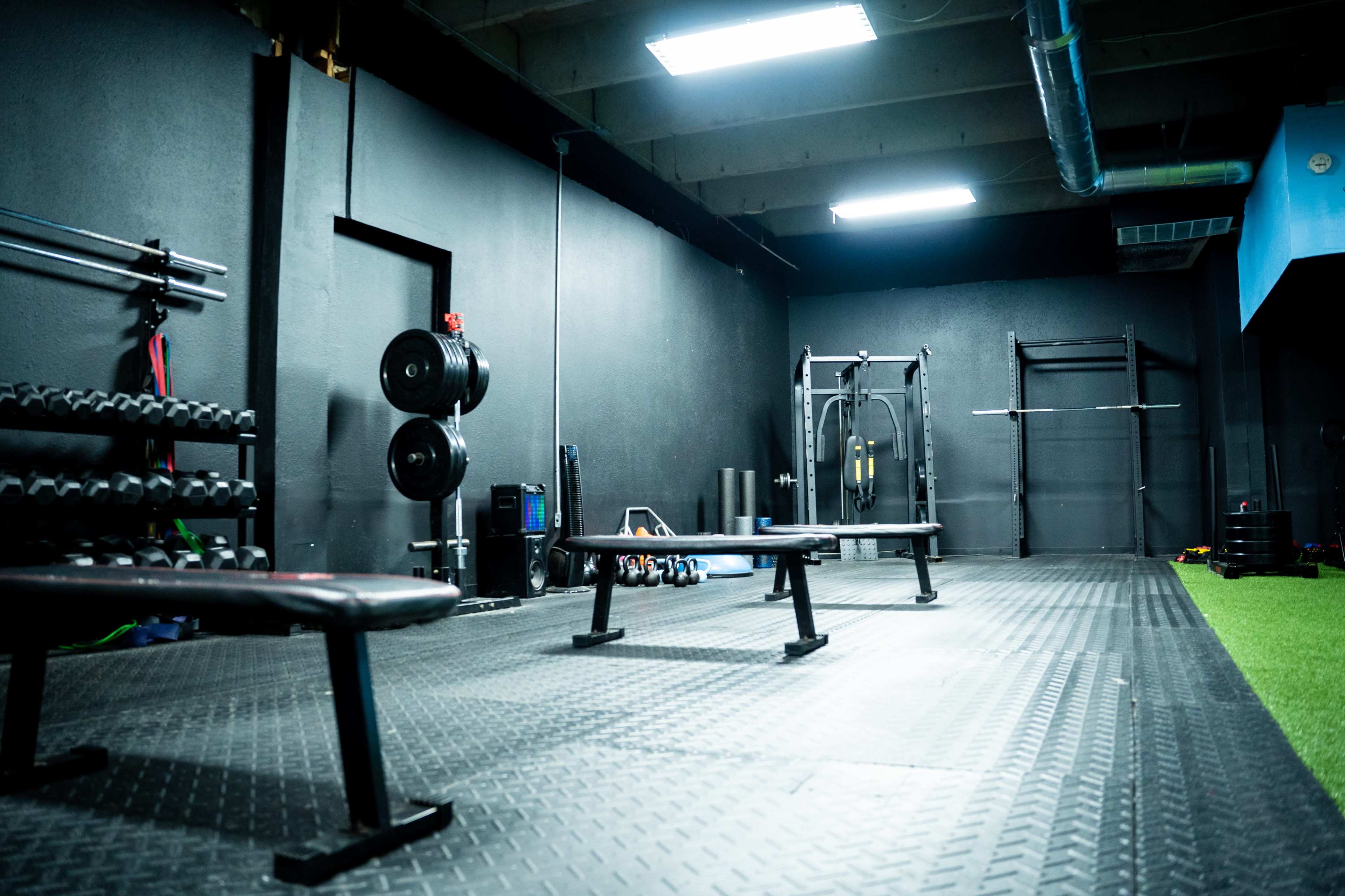 A fitness gym with dumbbells on a rack, benches, and exercise equipment on a textured black floor.