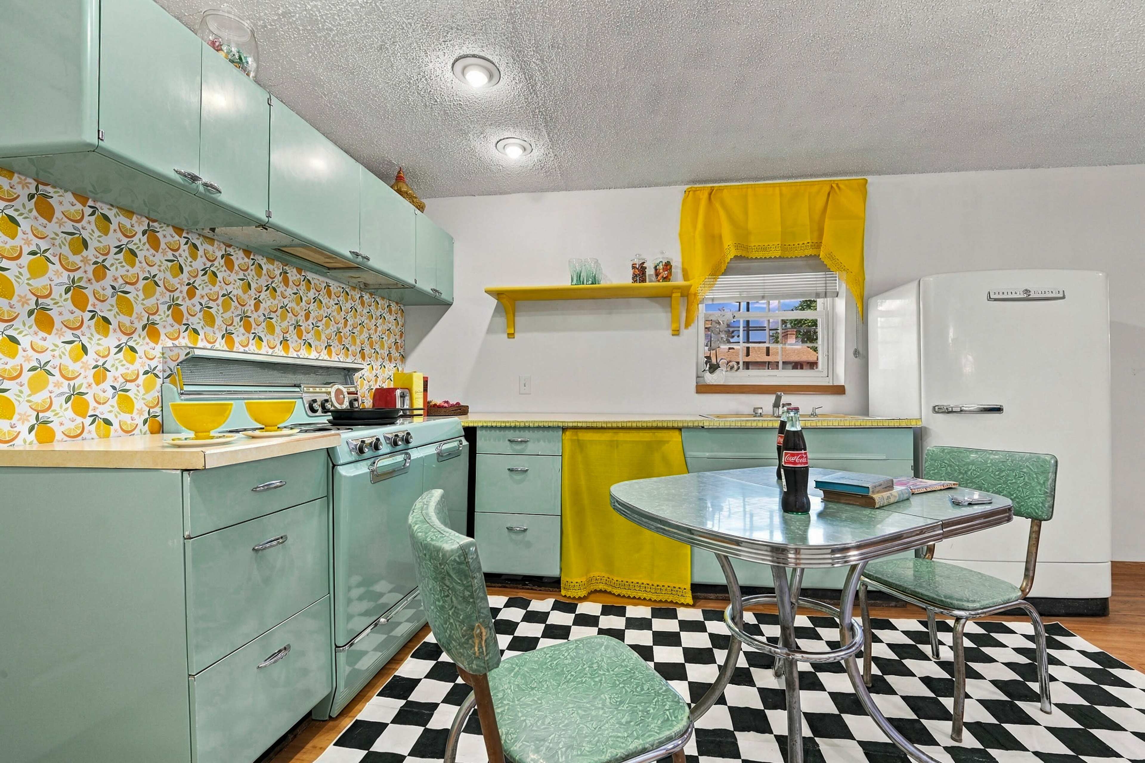 The image shows a retro-style kitchen with mint green cabinets, a round table, and a checkered black and white floor.