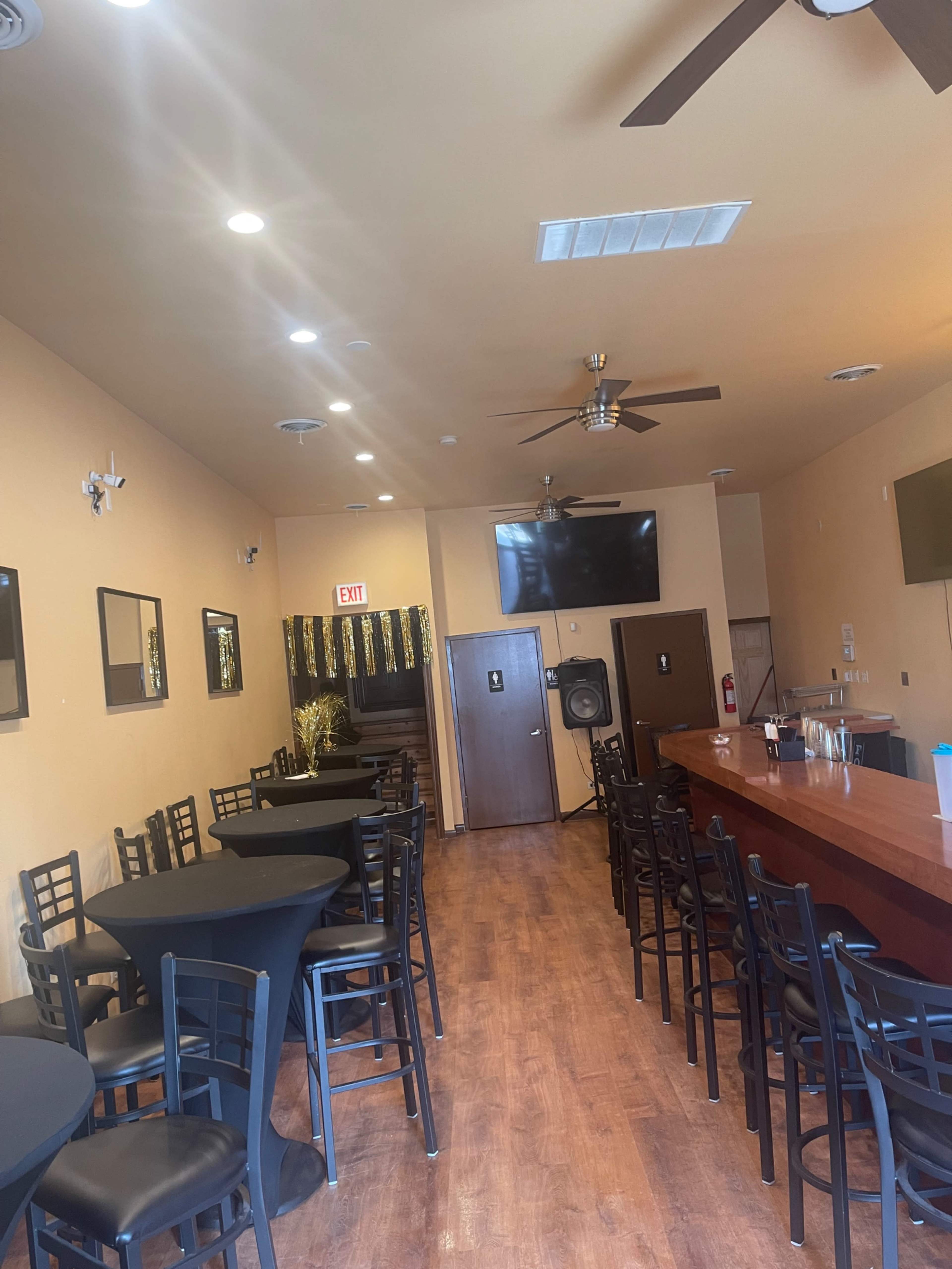 An empty bar area with a wooden counter and black tables and chairs arranged along the walls.