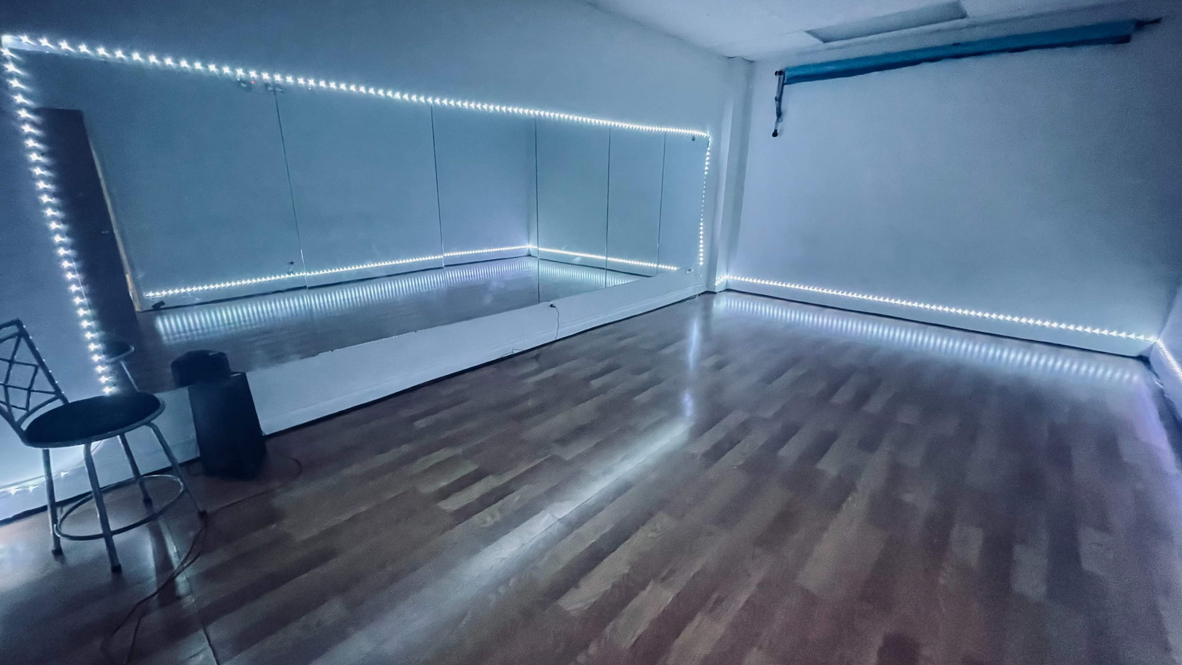 A dance studio with wooden flooring, a wall of mirrors, and LED lights along the edges.