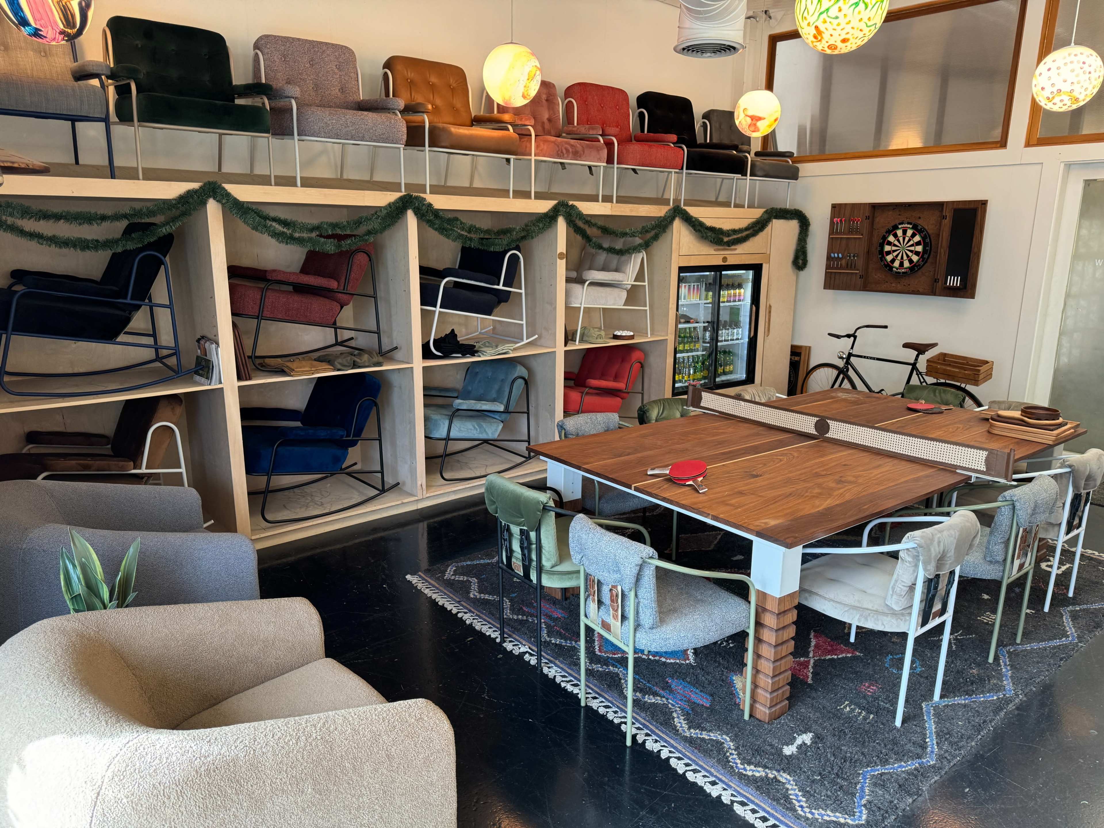 A cozy game room featuring a large wooden table surrounded by various chairs, a dartboard on the wall, and colorful seating displayed on shelves above.