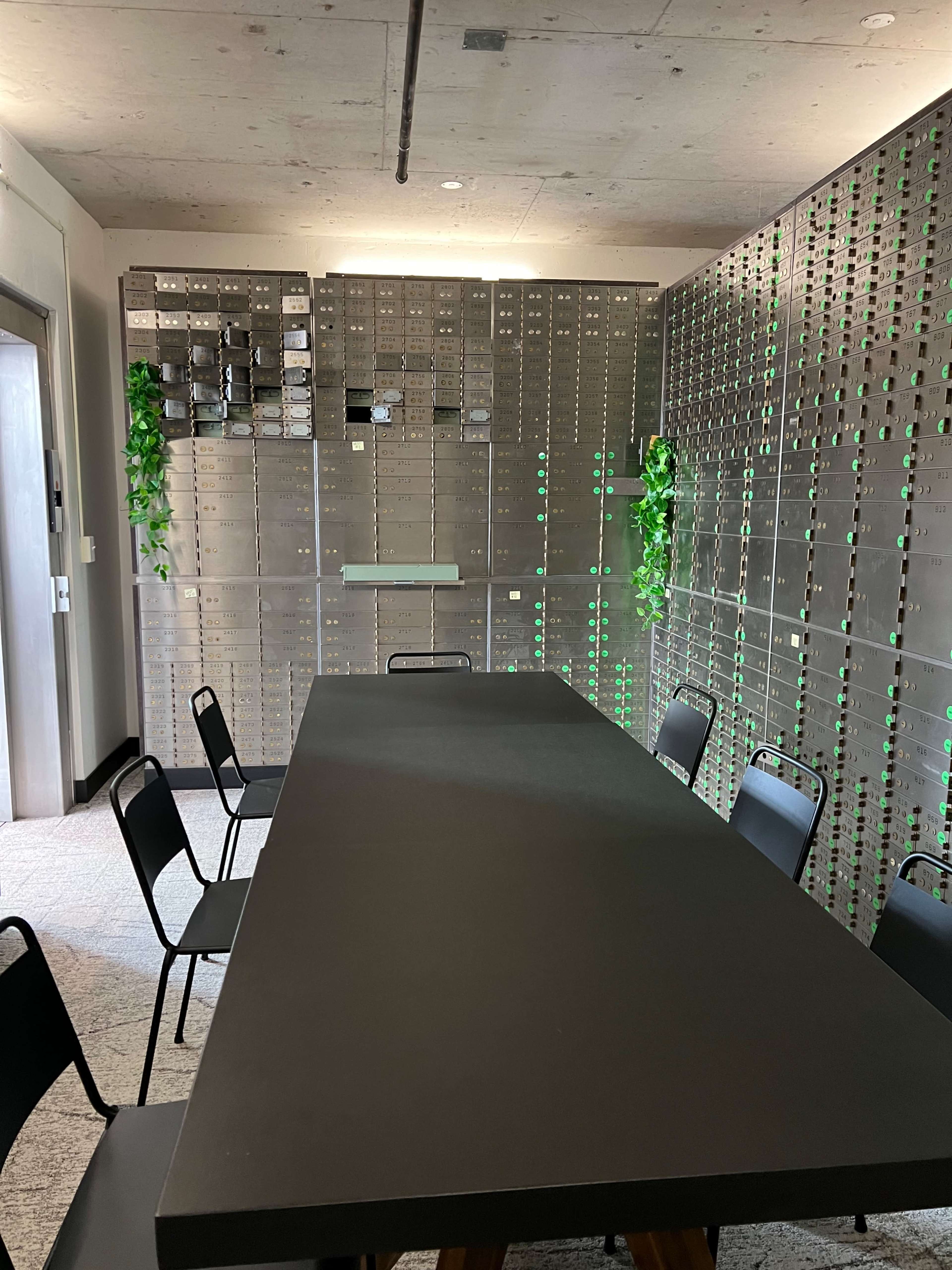 A conference room features a long black table surrounded by black chairs and a wall of green-lit lockers.