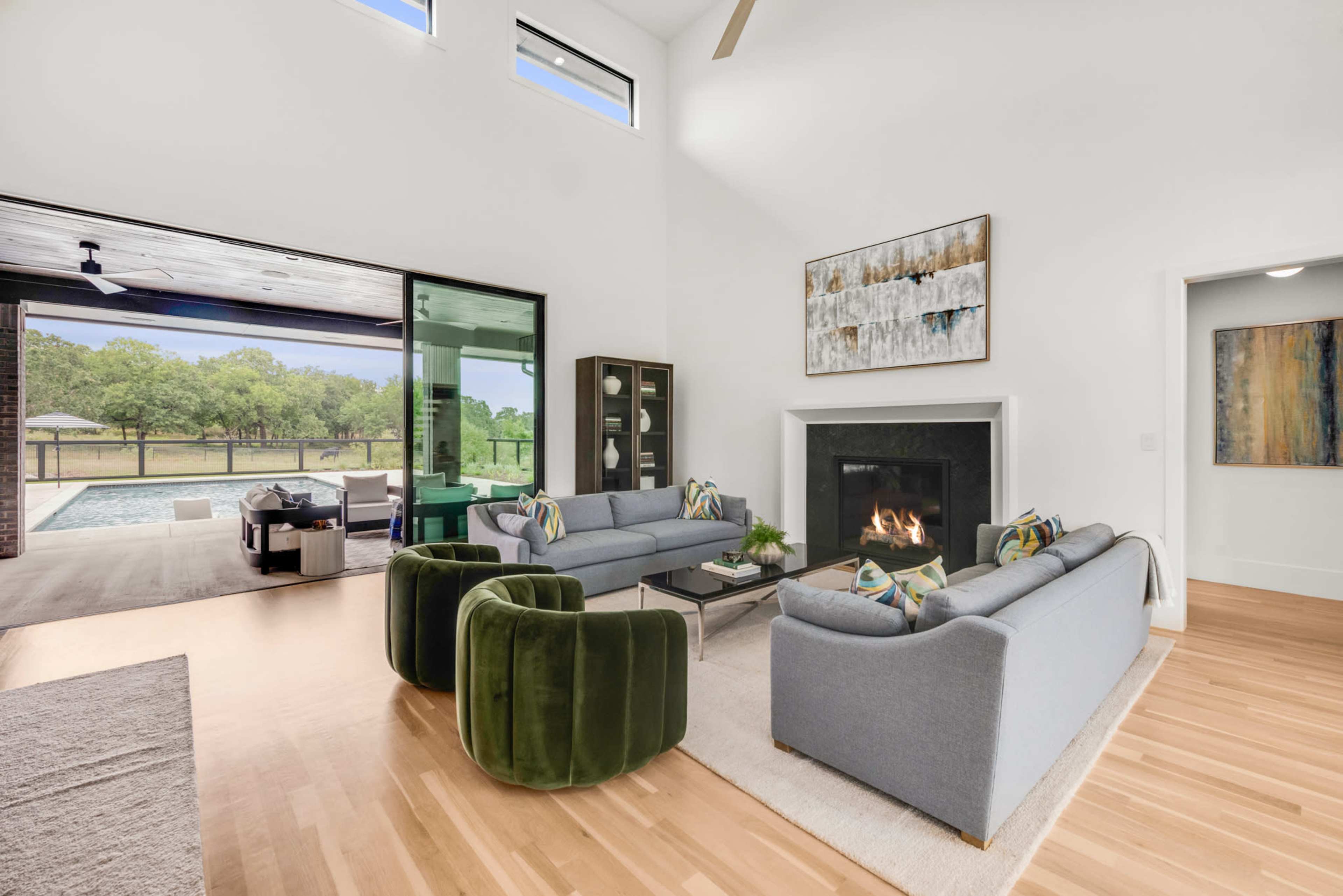 The spacious living room features two sofas and a pair of green chairs arranged around a fireplace, with large windows allowing natural light to illuminate the area.