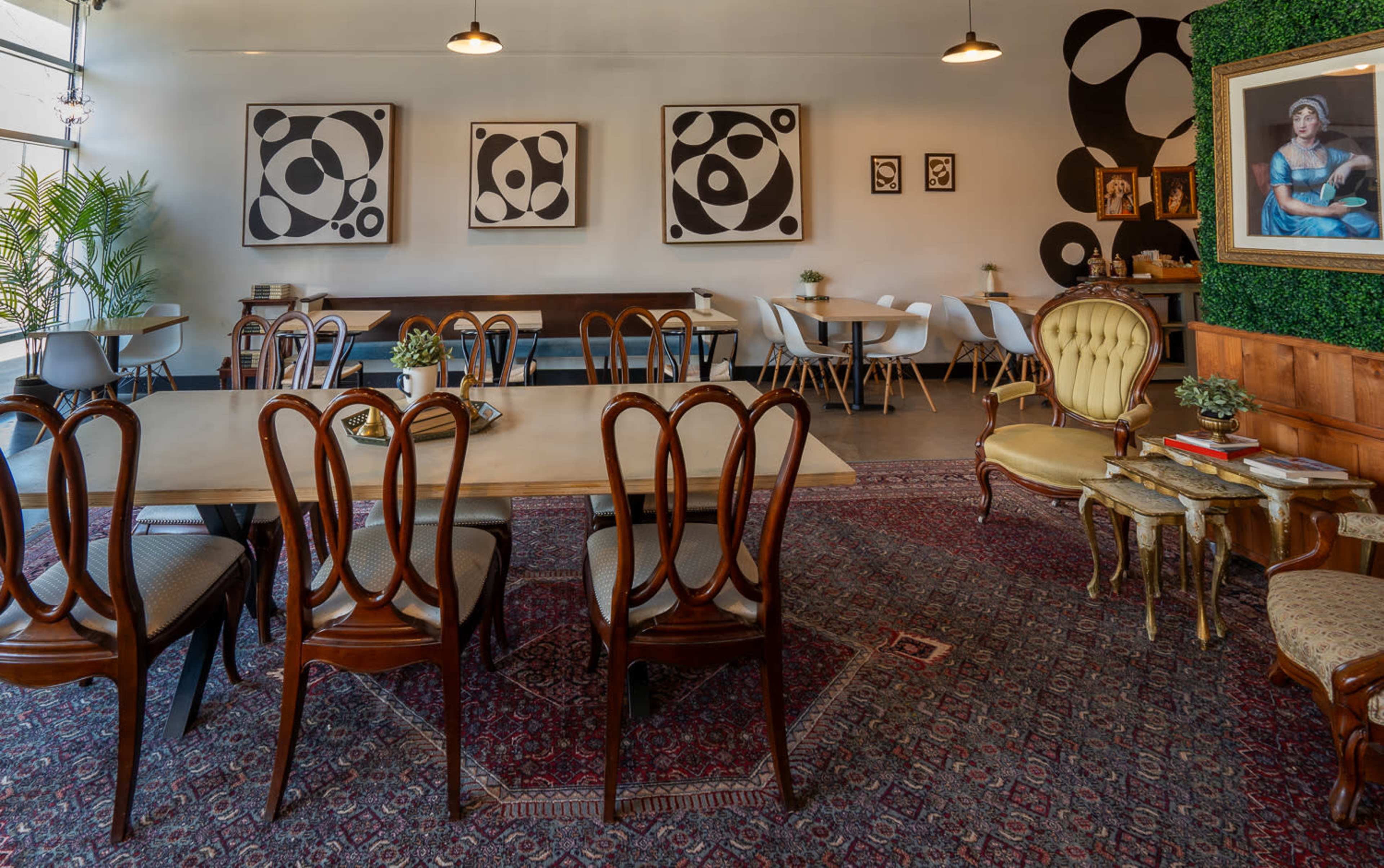A modern café interior with wooden tables, stylish chairs, abstract wall art, and a mix of seating arrangements.
