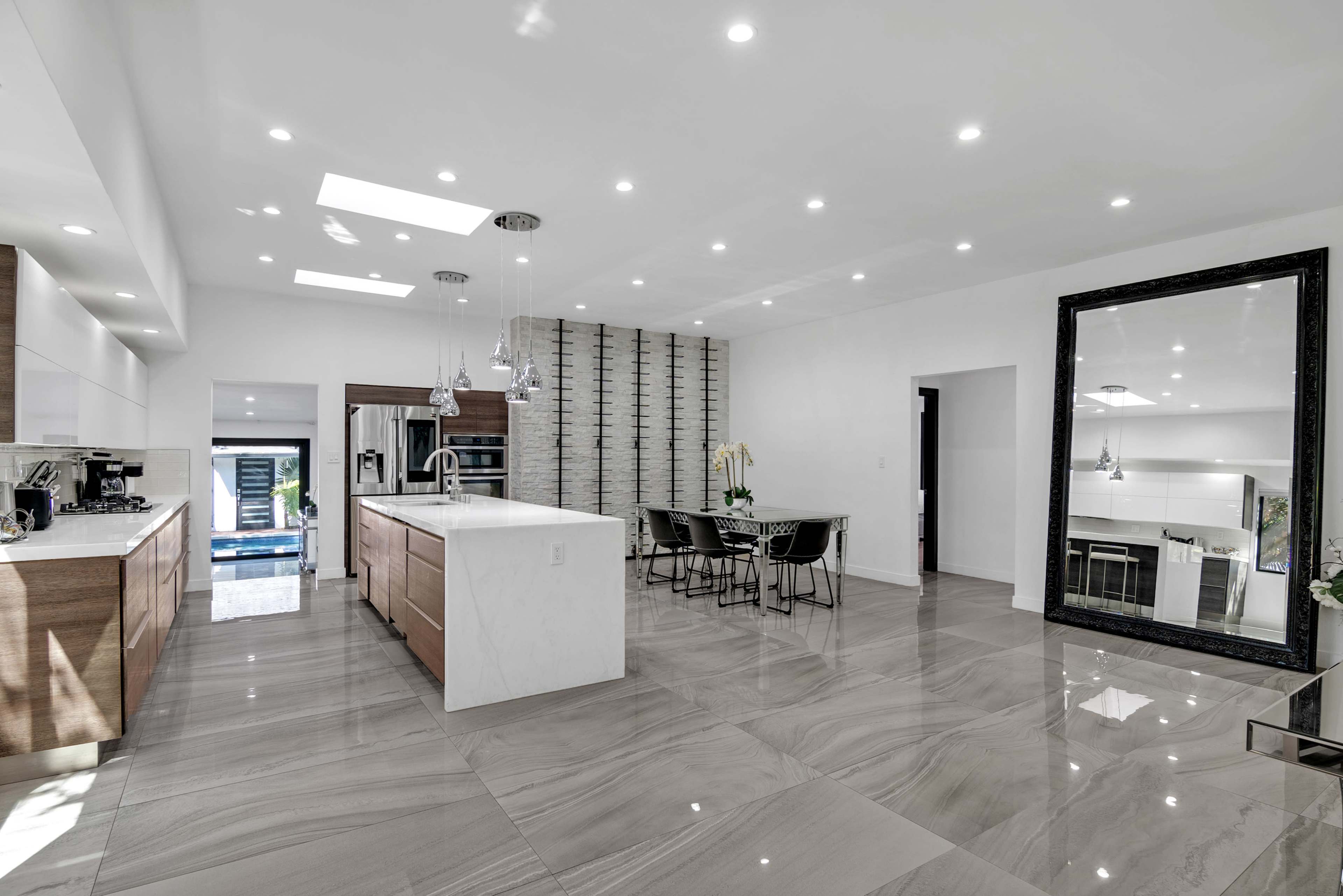 A modern kitchen with an open layout featuring a large island, sleek cabinetry, and a dining area with a glass table.