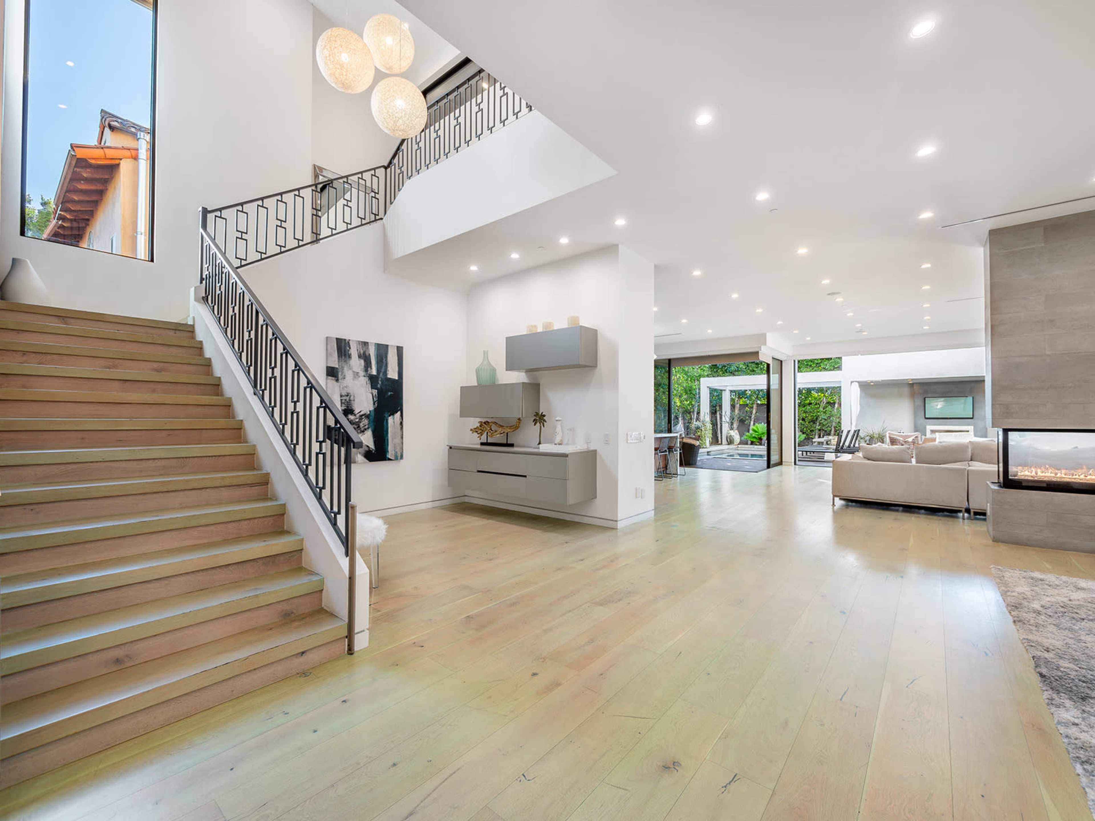 A modern interior space with a staircase, leading to an open living area that features large glass doors opening to an outdoor patio.