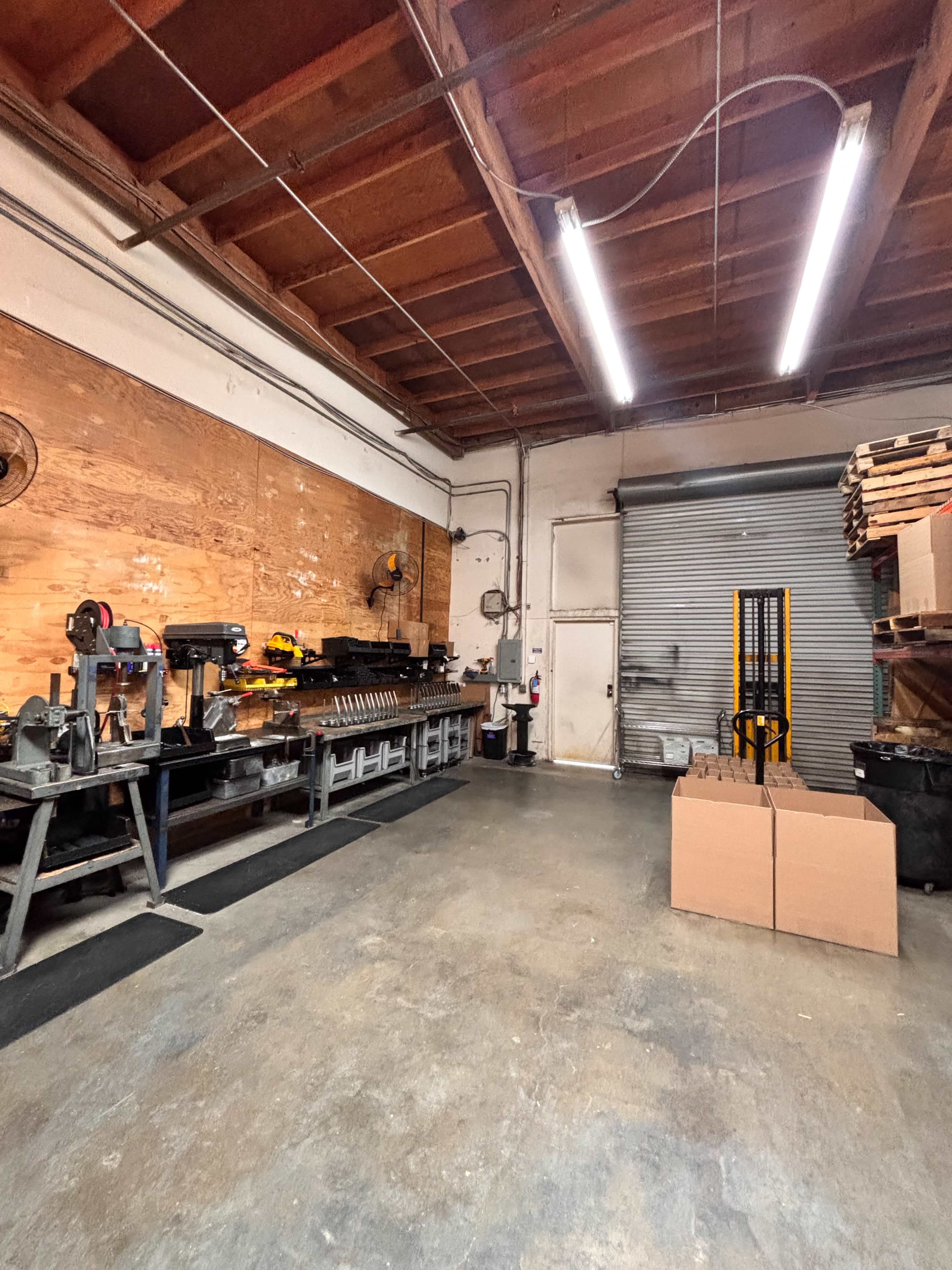 The image shows an industrial workshop with wooden walls, a workbench along one side, and a loading dock door at the far end.
