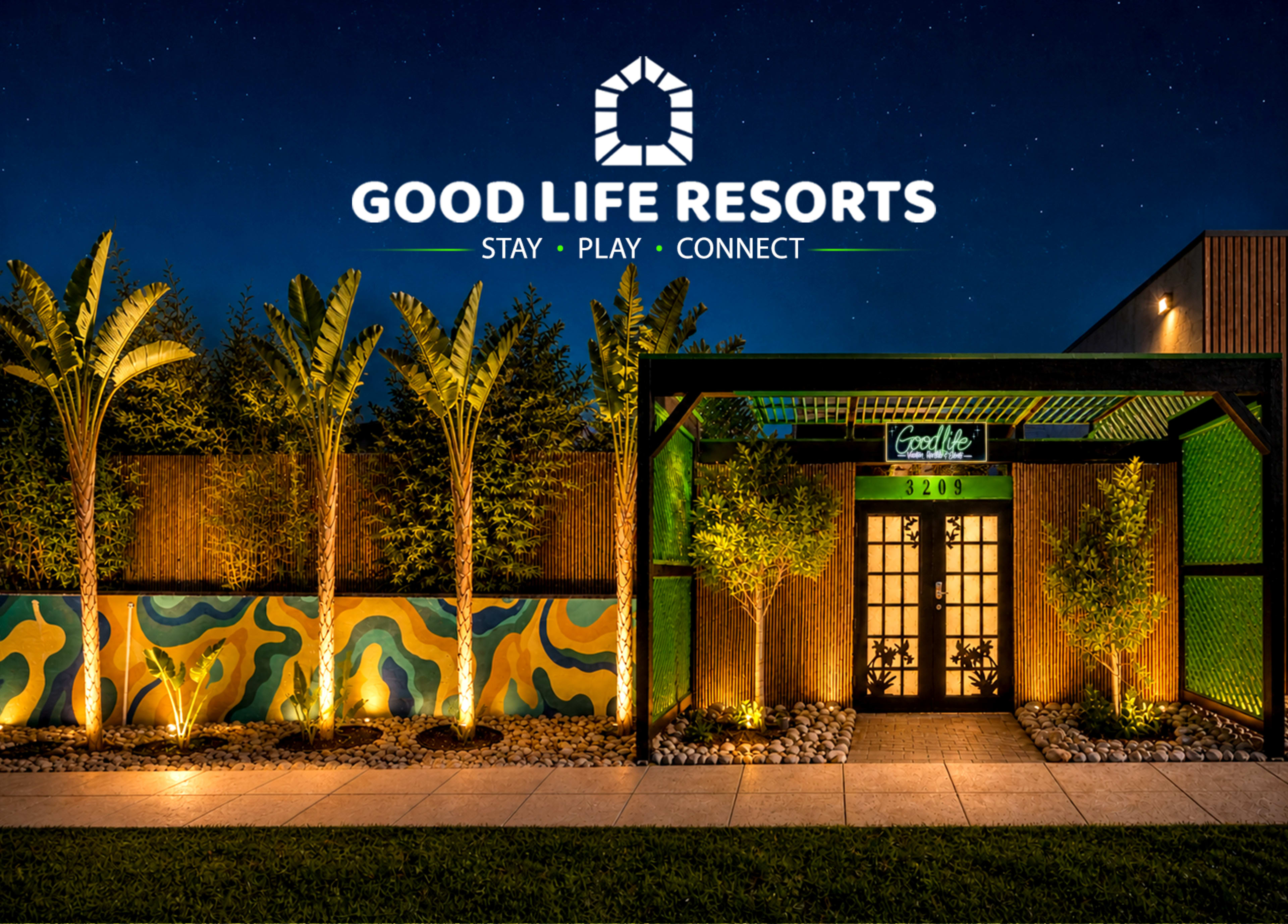 The image shows the entrance of Good Life Resorts, featuring a decorative facade with palm trees, a vibrant mural, and illuminated landscaping under a night sky.