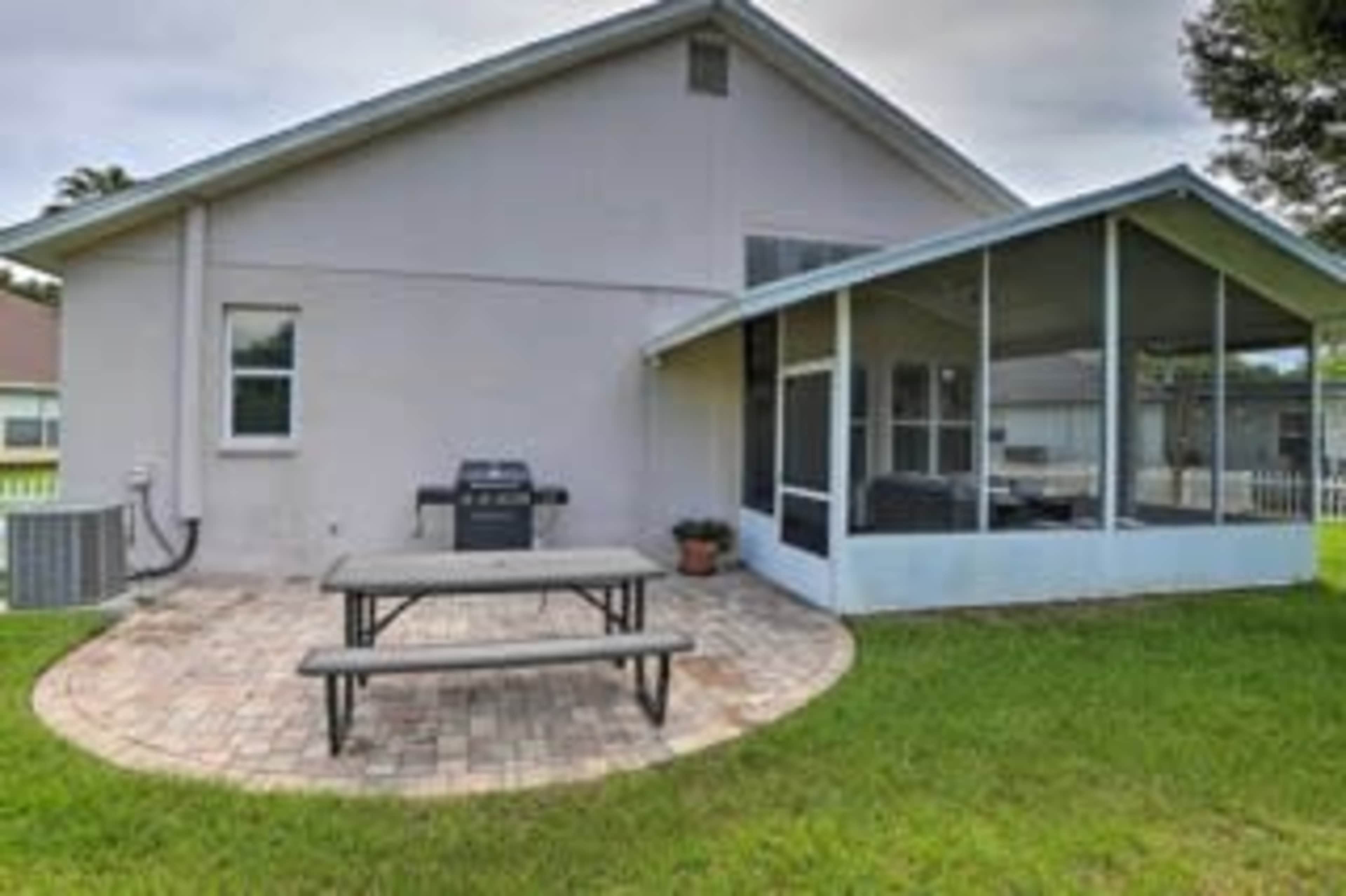 A backyard with a patio featuring a picnic table and a grill, adjacent to a screened porch.