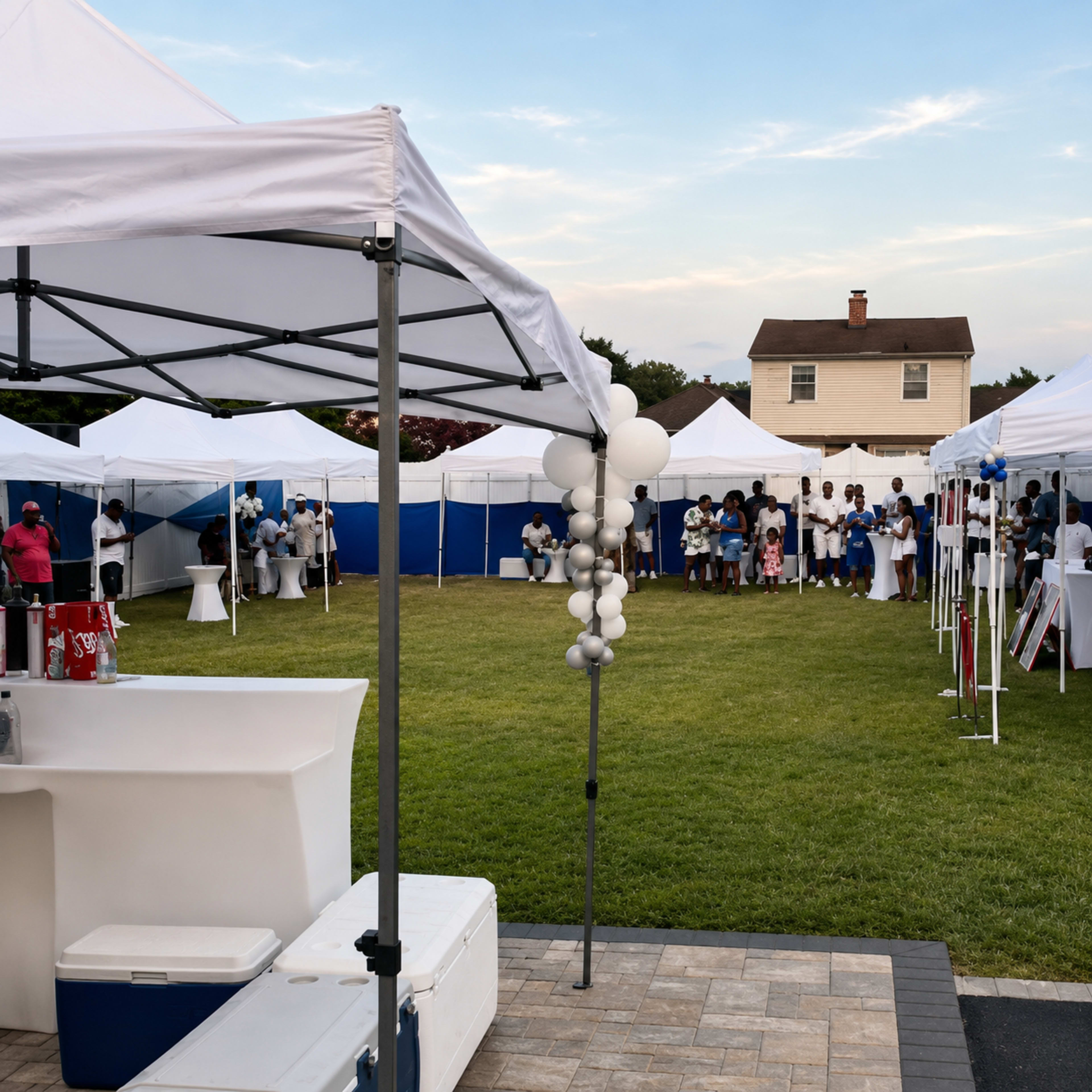 A large outdoor event features several white tents set up on green grass, with guests mingling and socializing in the background.