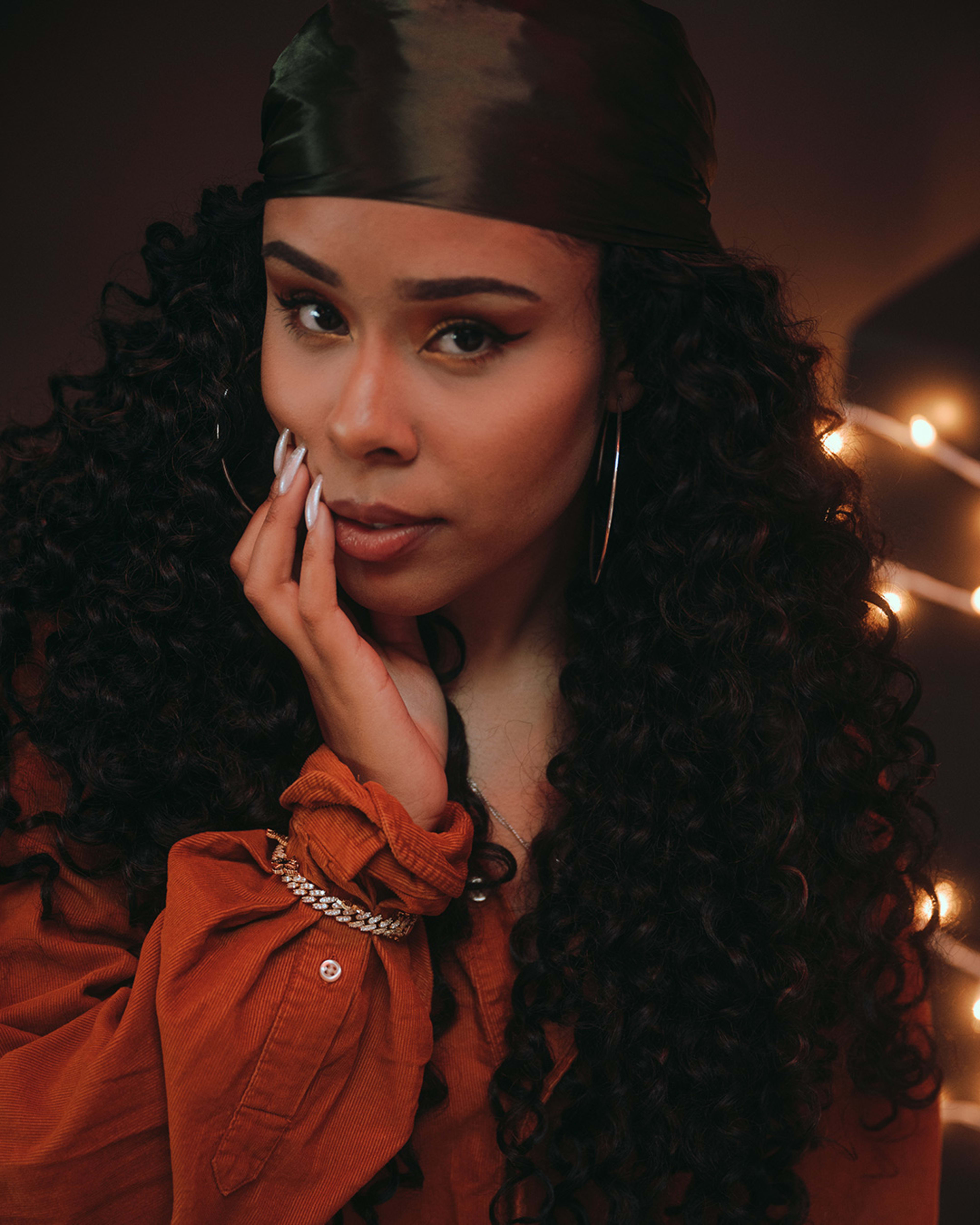 A brown-skinned woman with long curly hair in a photo shoot.